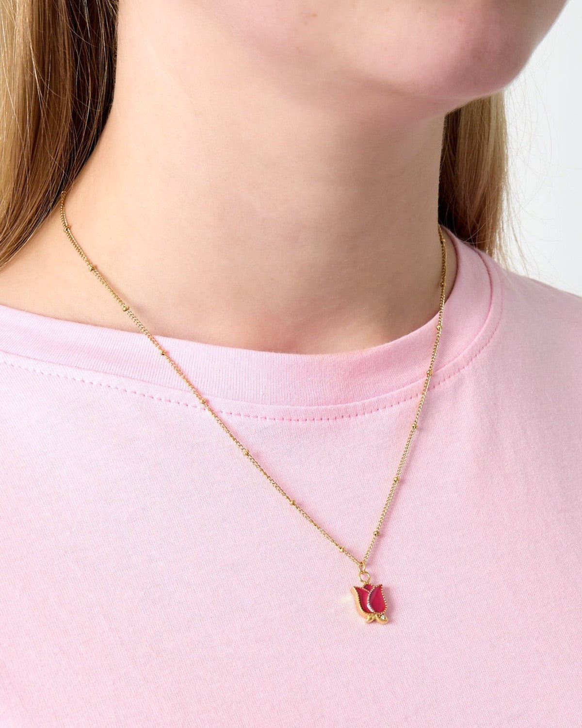Close-up of a woman wearing a gold-tone necklace with a red enamel rose pendant over a pink t-shirt