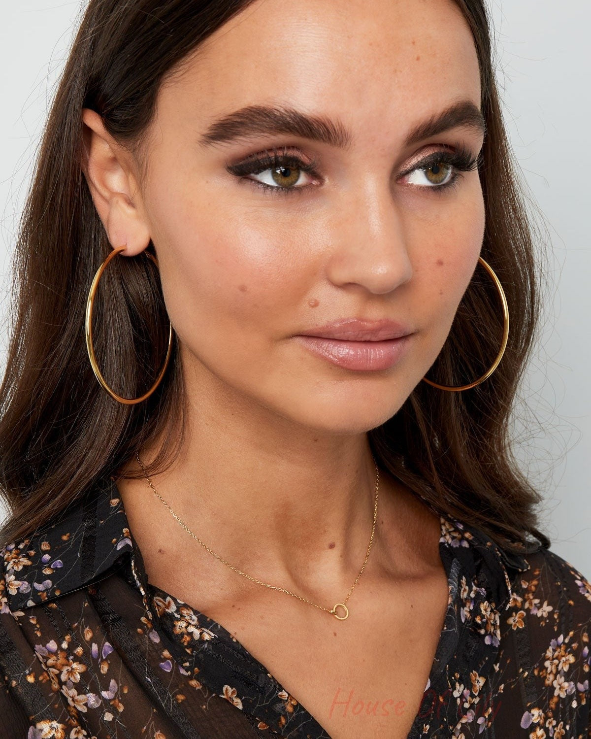 Model wearing the delicate gold linked circle necklace and large hoop earrings, styled with floral black blouse