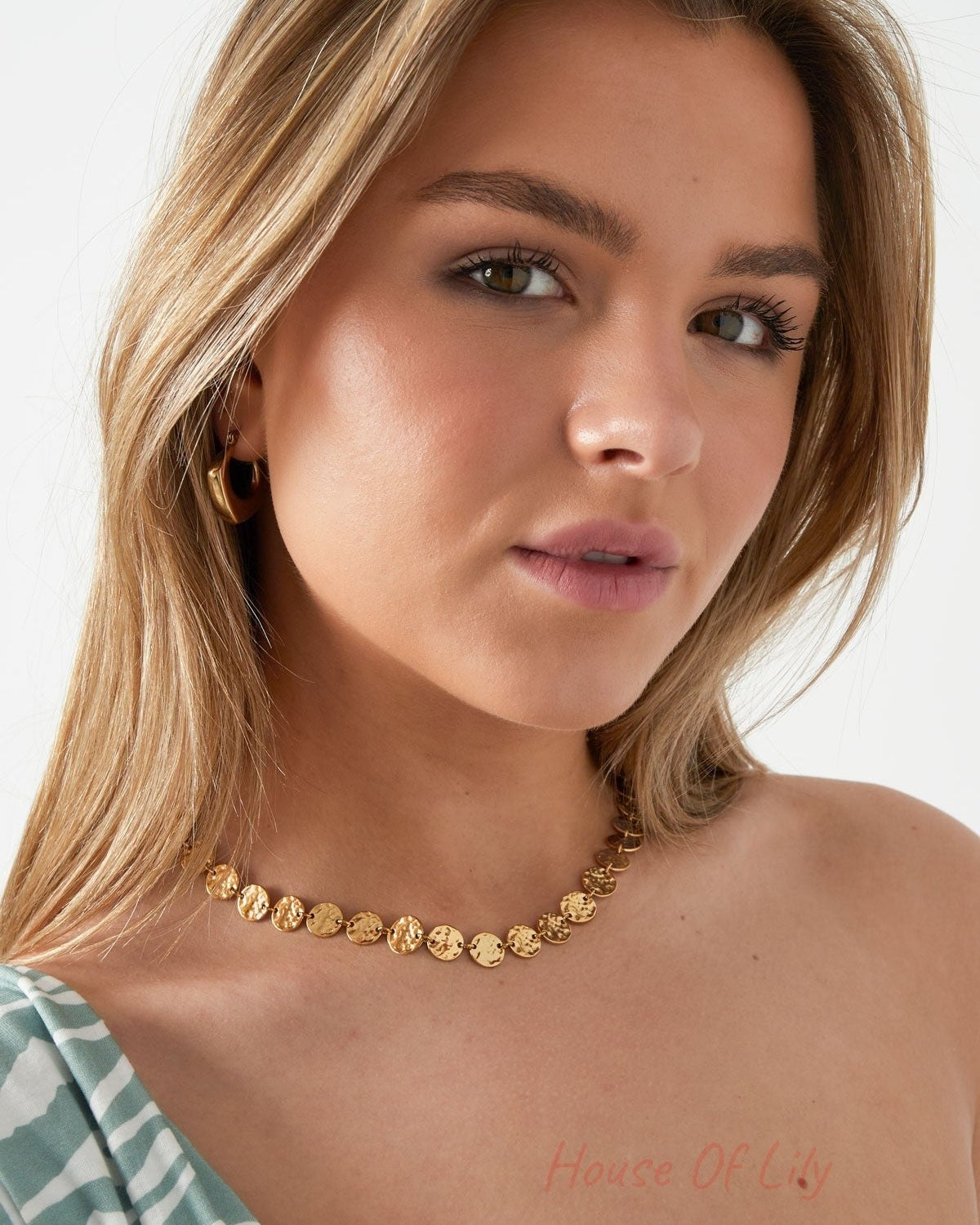 Model wearing the hammered gold disc necklace paired with gold hoop earrings and a striped off-shoulder top