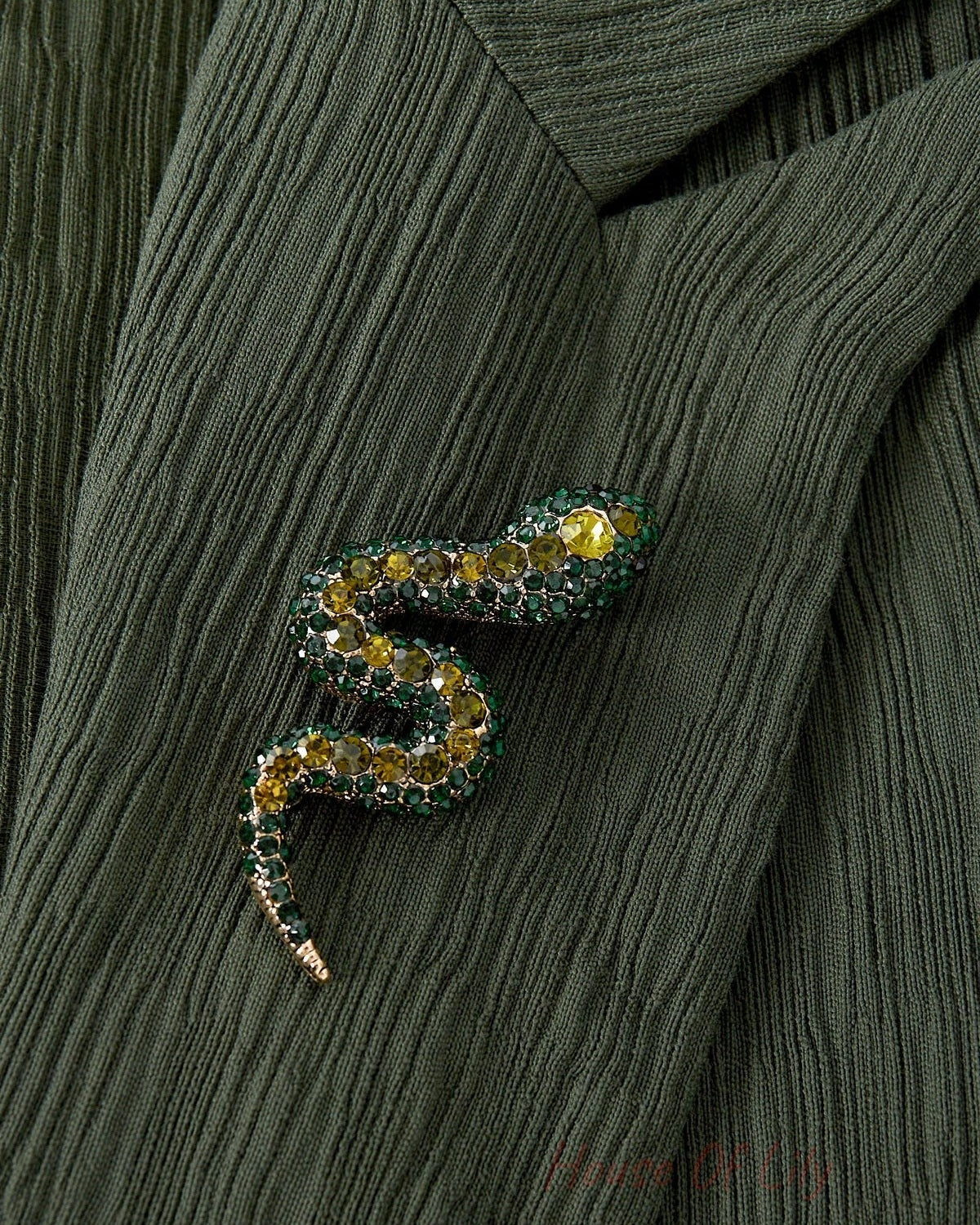 Close-up of green and yellow crystal snake brooch pinned to textured green fabric jacket