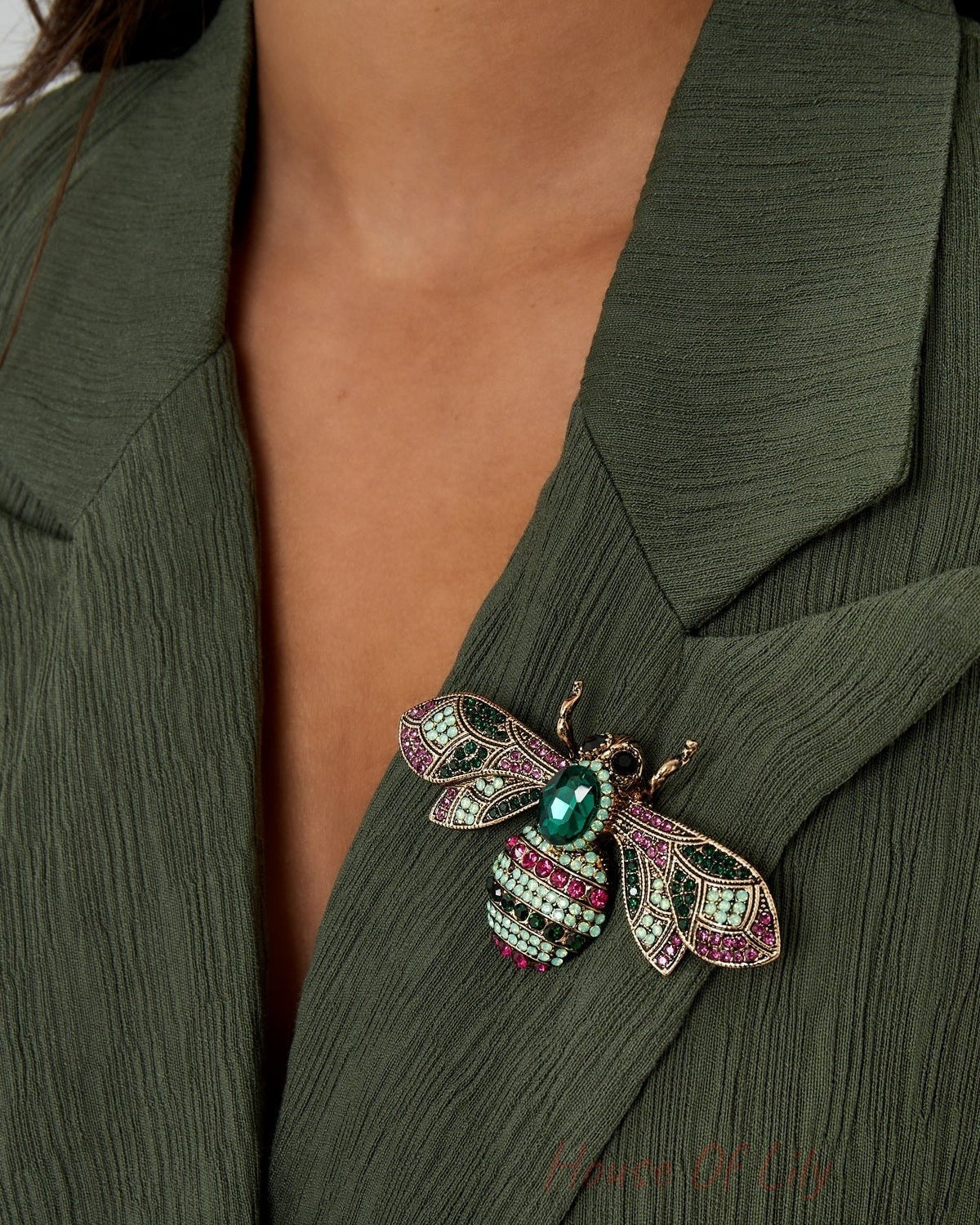 Woman wearing a green textured jacket with a gemstone bee brooch pinned on the lapel