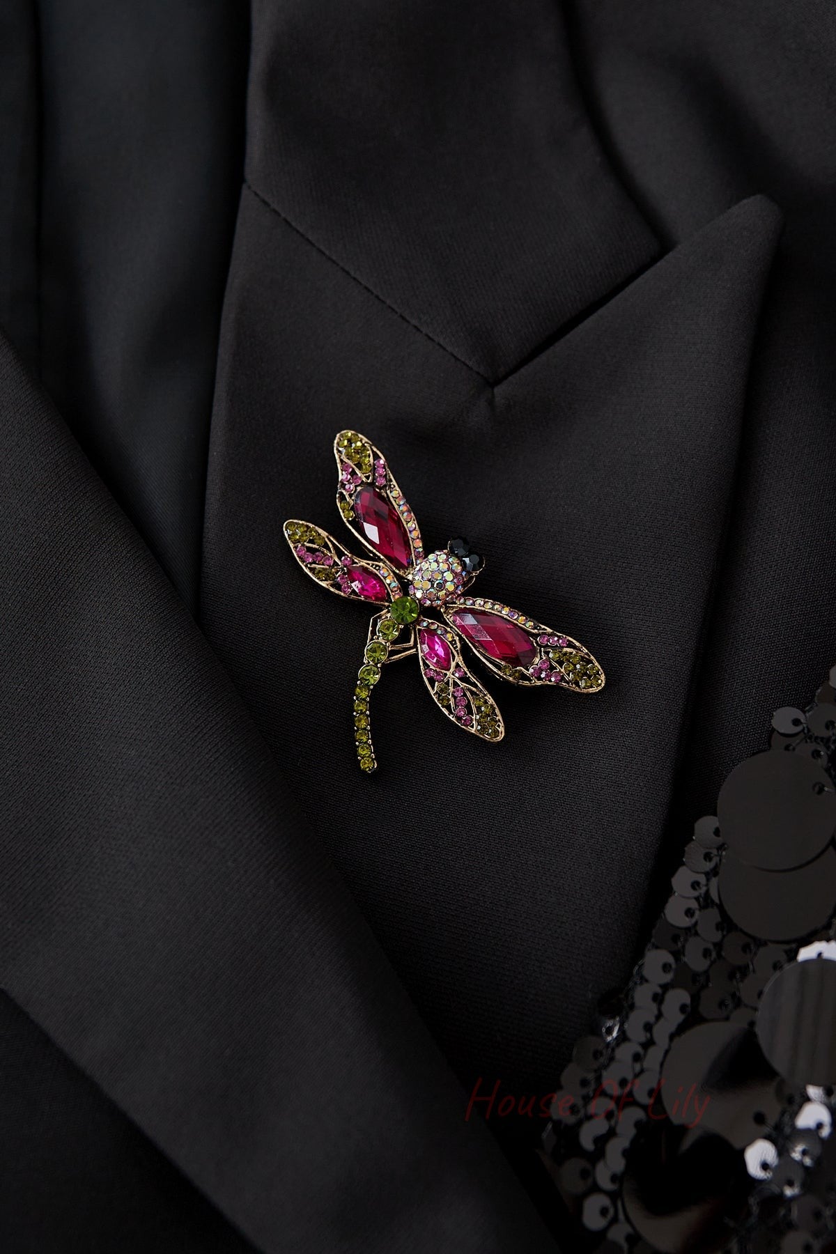 Dragonfly brooch pinned on black fabric jacket, showcasing its vibrant pink, red, and green stones