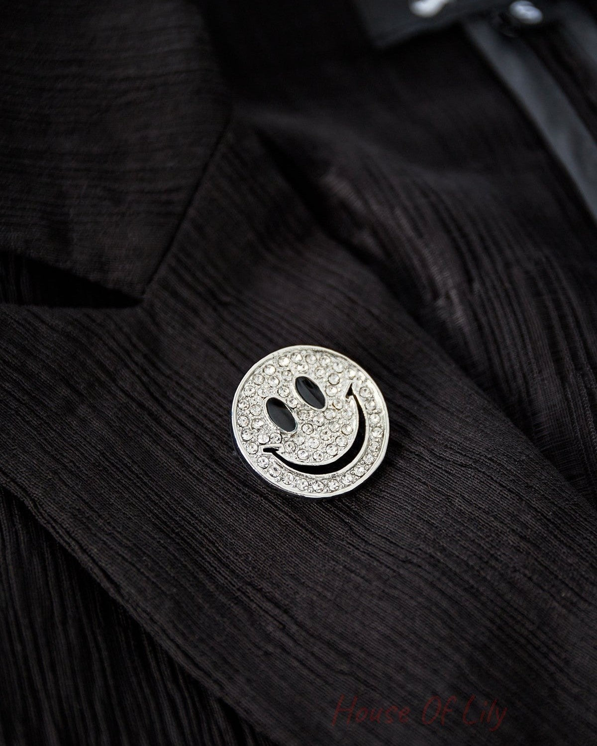 Silver-tone smiley face brooch with clear crystals pinned to a black textured jacket