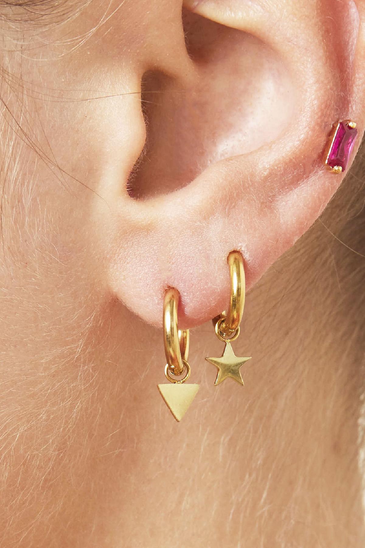 Close-up of two gold hoop earrings with star and triangle charms worn on pierced ear