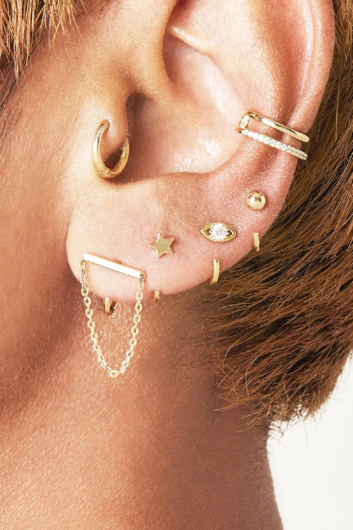 Close-up of ear with multiple gold-tone earrings and a double band gold and crystal ear cuff clipped to the upper ear