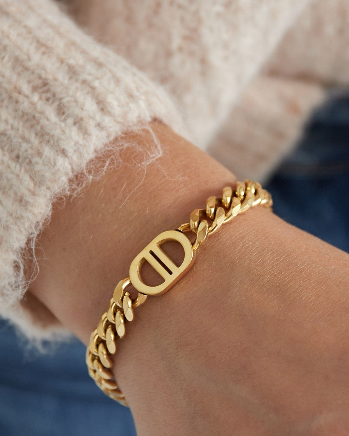 Gold chunky chain link bracelet on wrist with cream sweater and blue jeans showcasing the oval dual-bar centerpiece