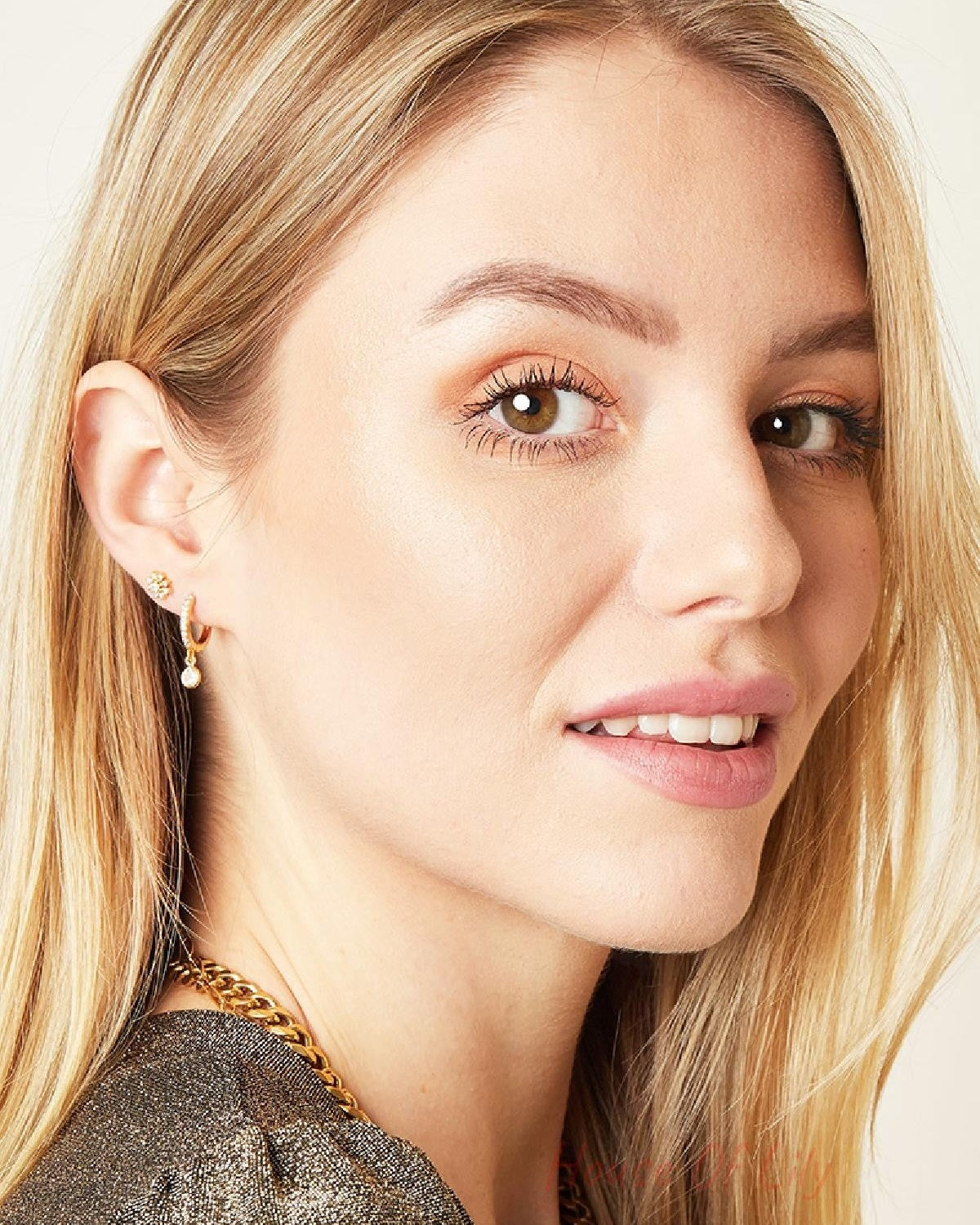 Portrait of a smiling woman with blonde hair wearing the gold crystal flower piercing earring alongside a stylish gold chain necklace
