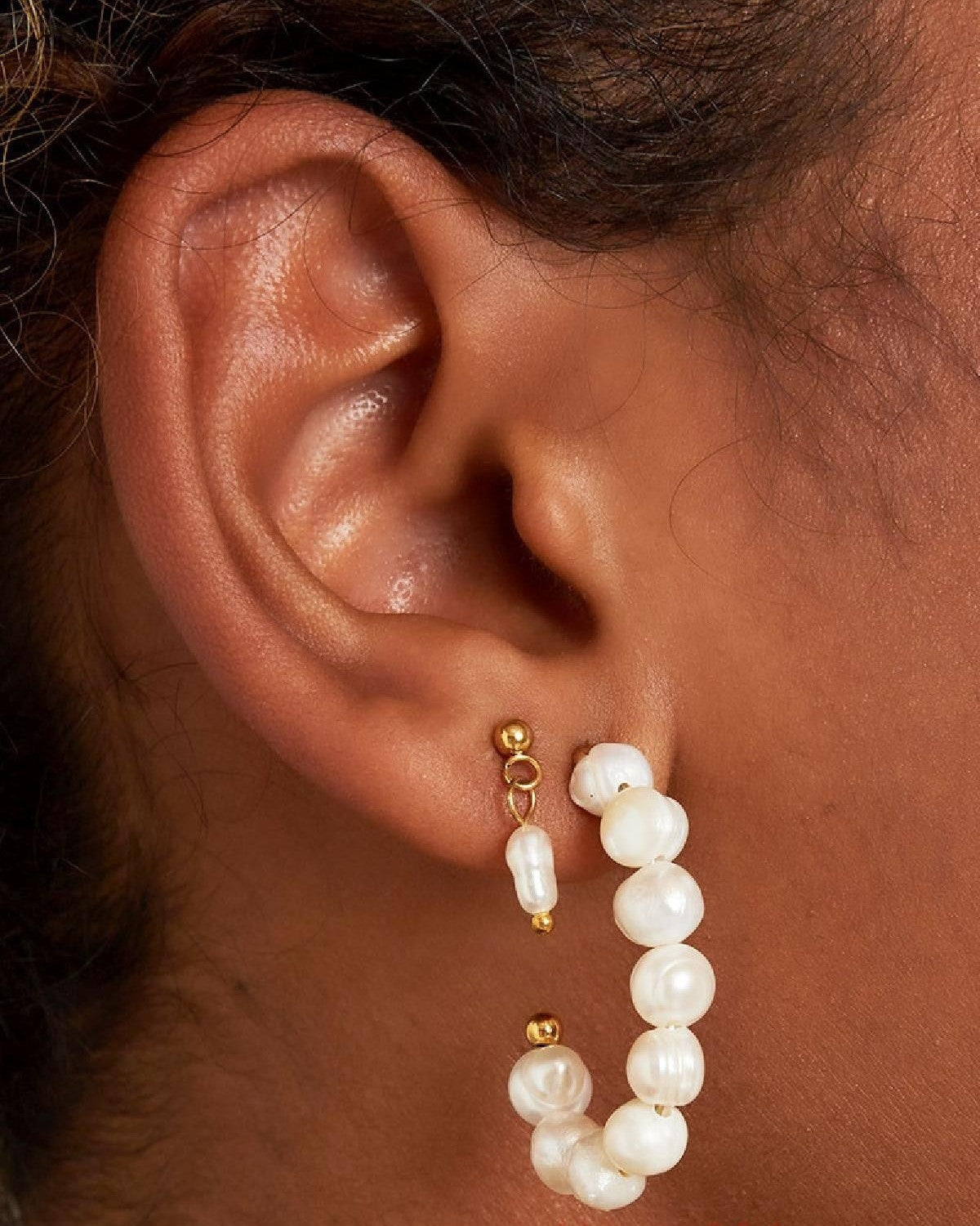 Close-up of ear wearing gold-tone short drop earrings with tiny freshwater pearls and larger pearl hoop earring