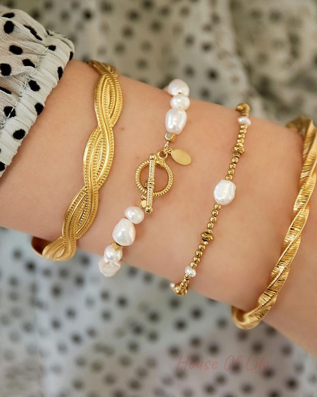 Wrist adorned with stacked bracelets including a pearl beaded bracelet with gold accents against polka dot sleeve