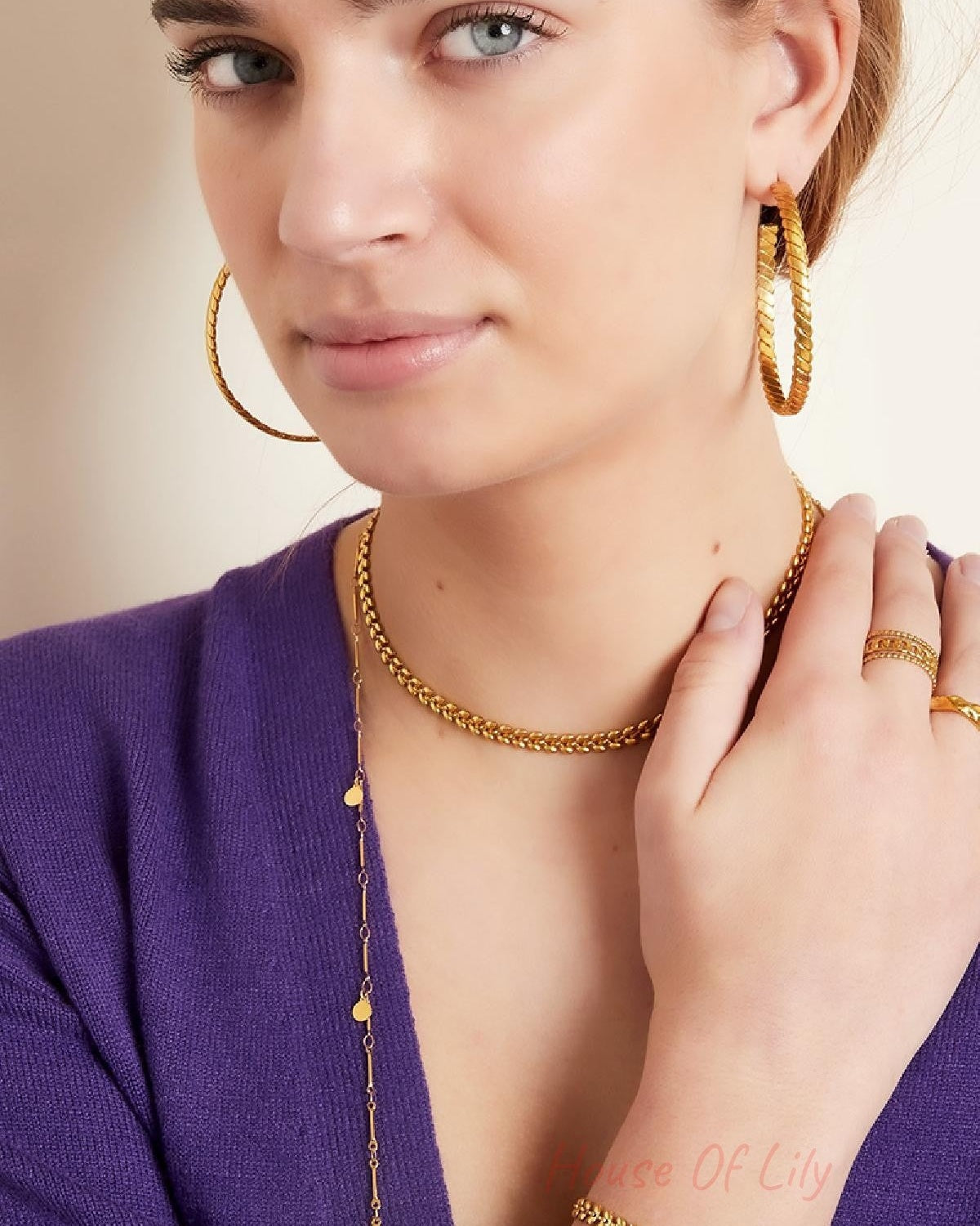 Close-up of model's face wearing gold leaf chain choker and leaf design hoop earrings with multiple bracelets