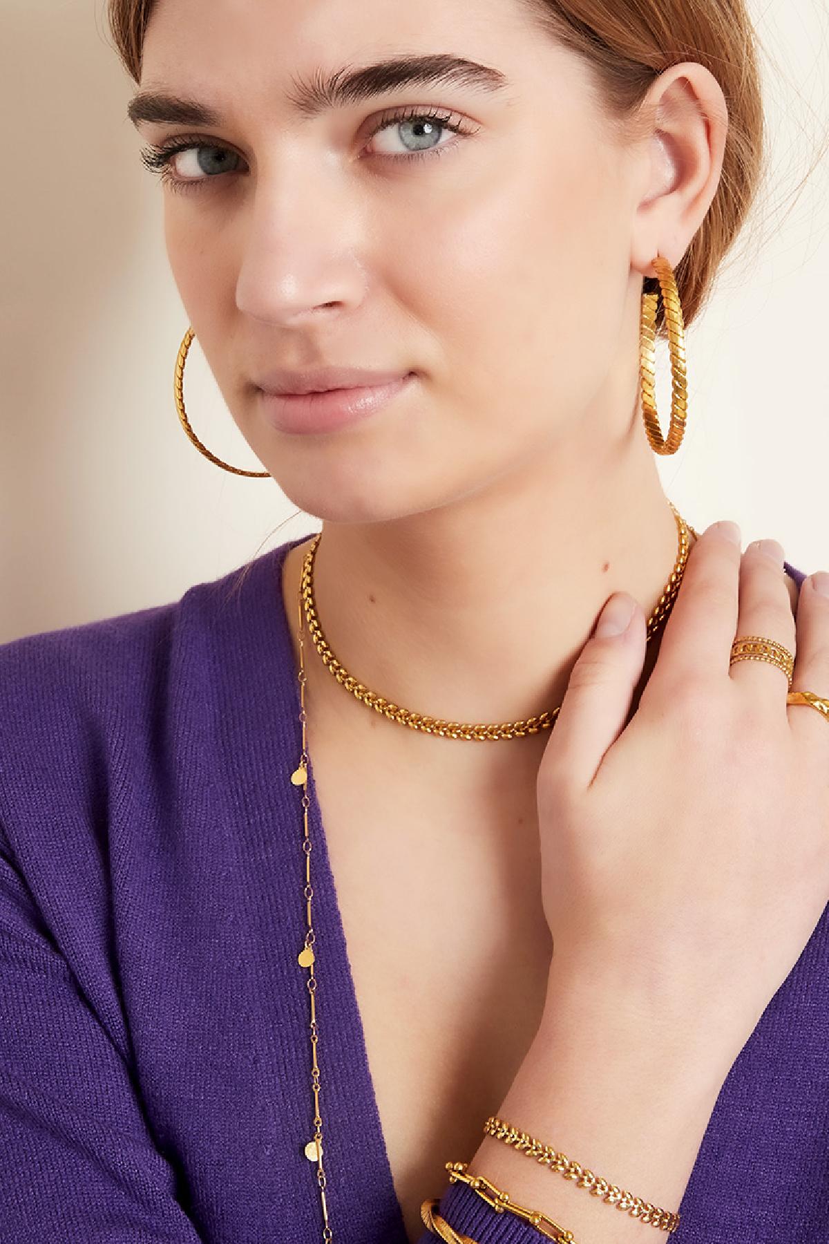 Close-up of model's face wearing gold leaf chain choker and leaf design hoop earrings with multiple bracelets