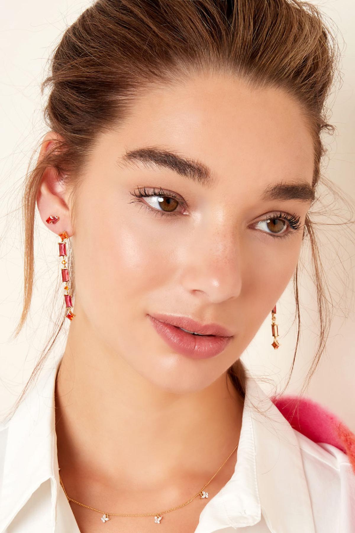 Portrait of a woman with subtle makeup wearing gold earrings with red and orange stones, styled for a youthful and aesthetic look.