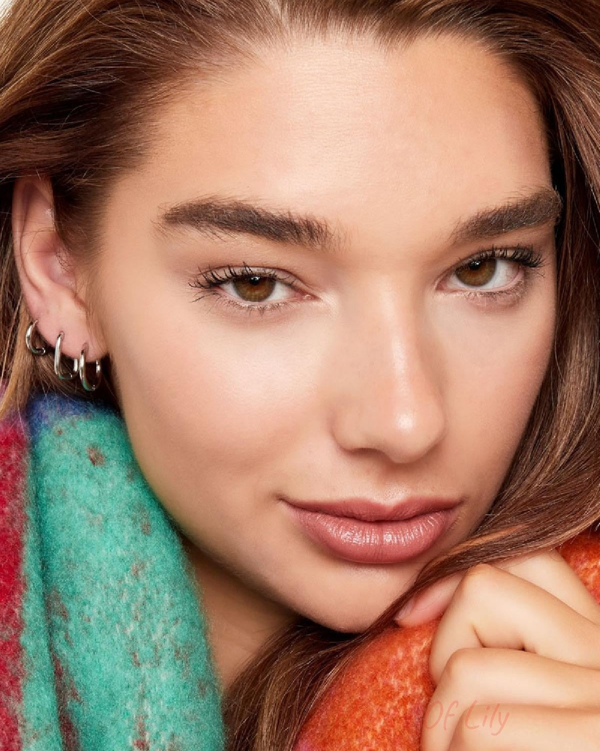 Close-up of ear with multiple small silver hoop earrings worn with colorful cozy scarf