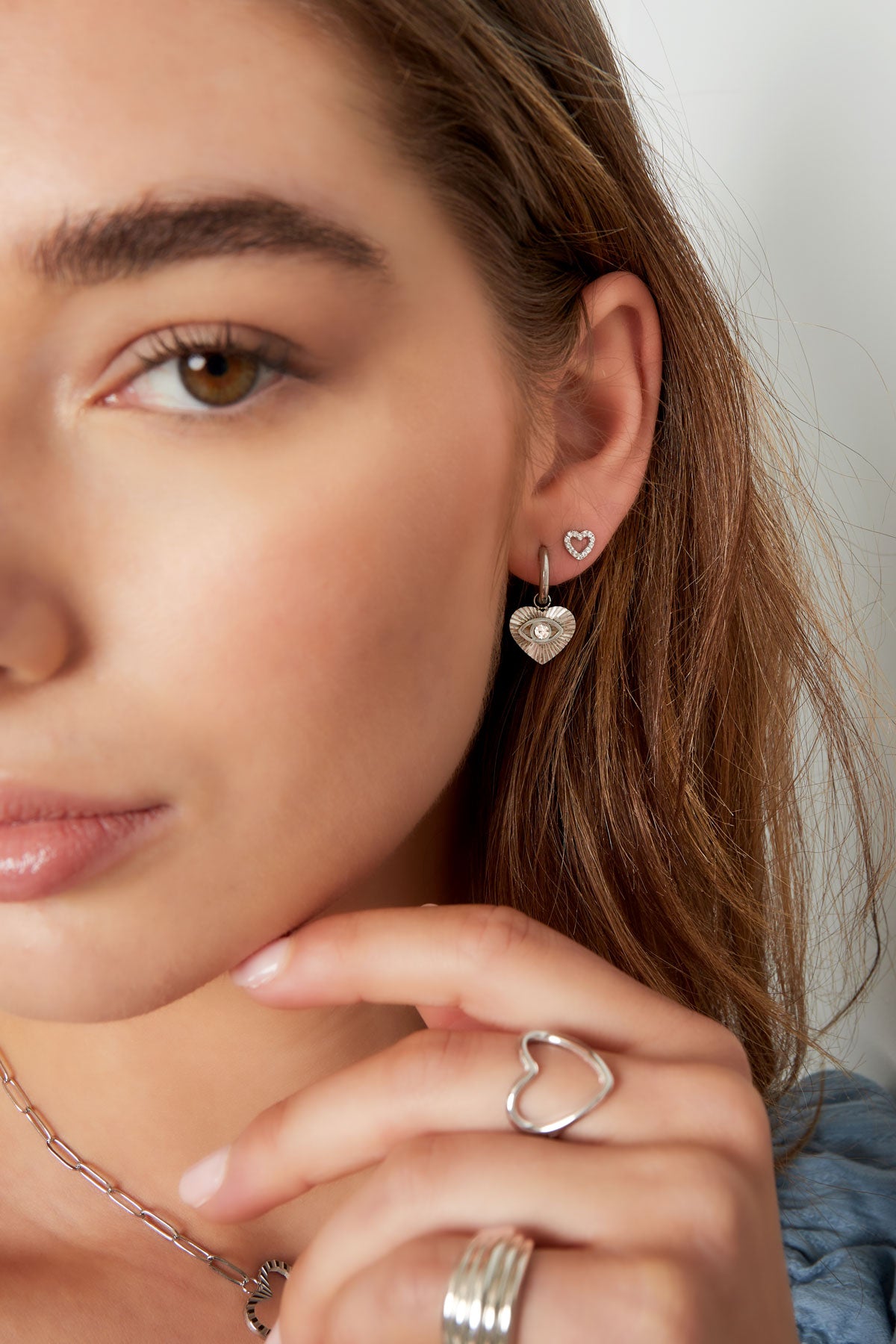 Woman’s face with visible gold rhinestone heart stud earring paired with silver heart hoop earrings and matching rings