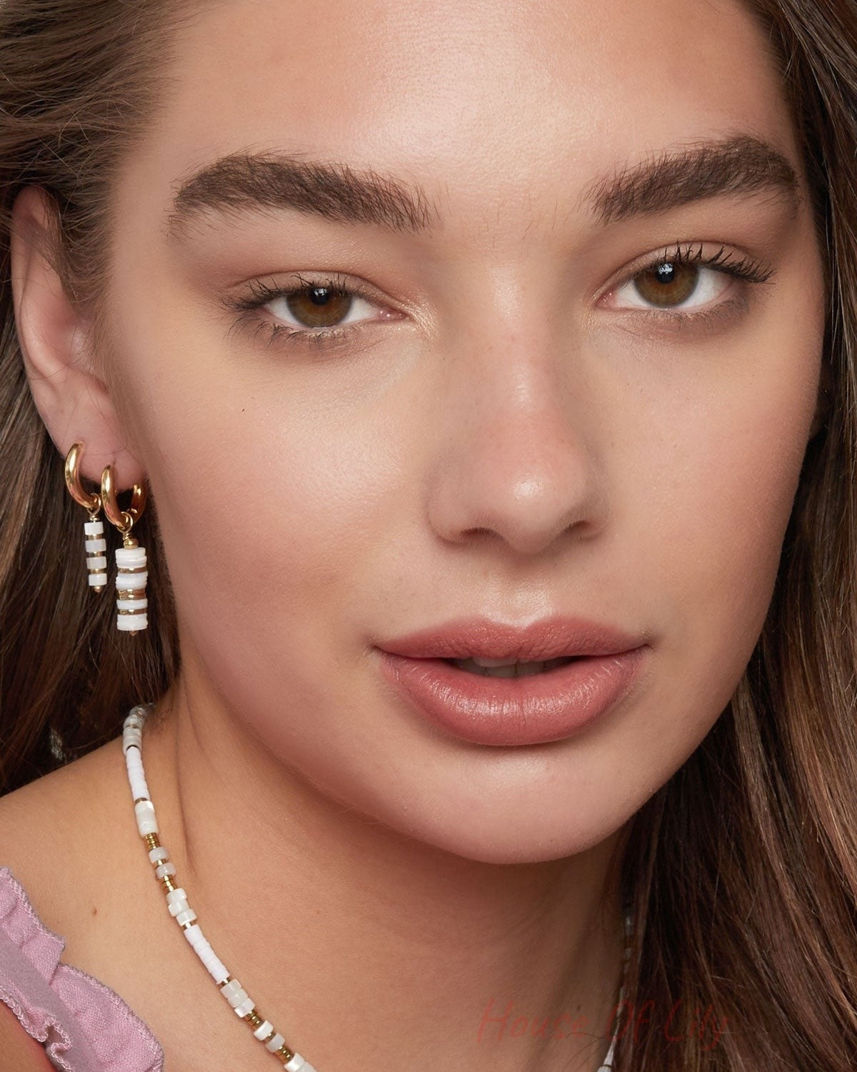 Front view of a woman wearing gold and white beaded hoop earrings and coordinating beaded necklace, showcasing youthful, minimal boutique style.
