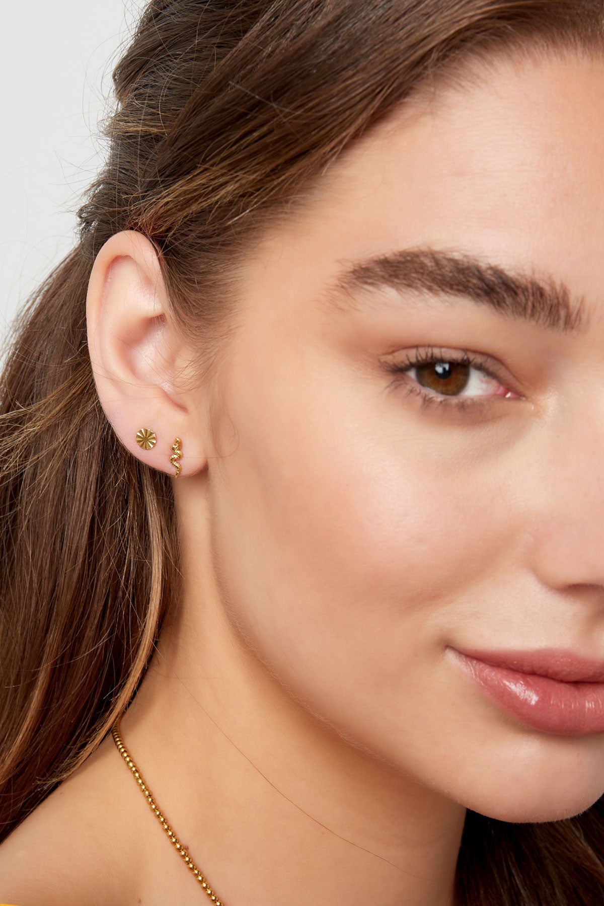 Side view of woman smiling, showcasing her gold snake stud earring and delicate jewelry