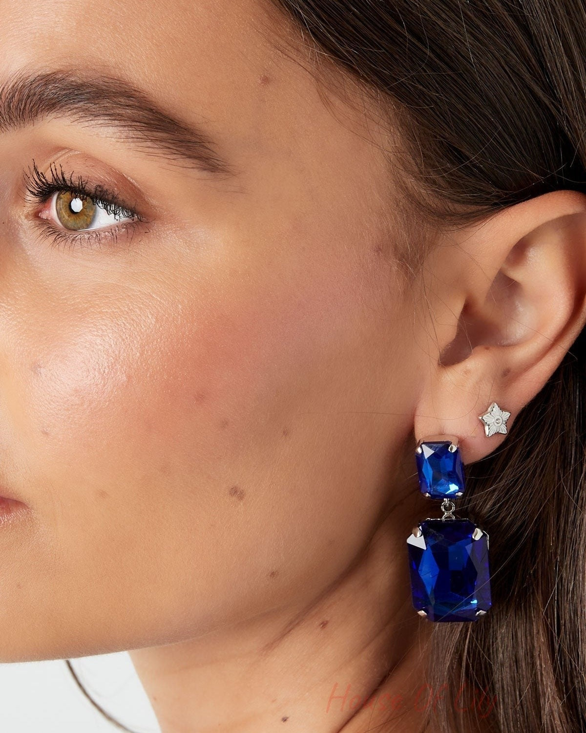 Model close-up showing silver star mini stud earring worn with large blue statement earrings