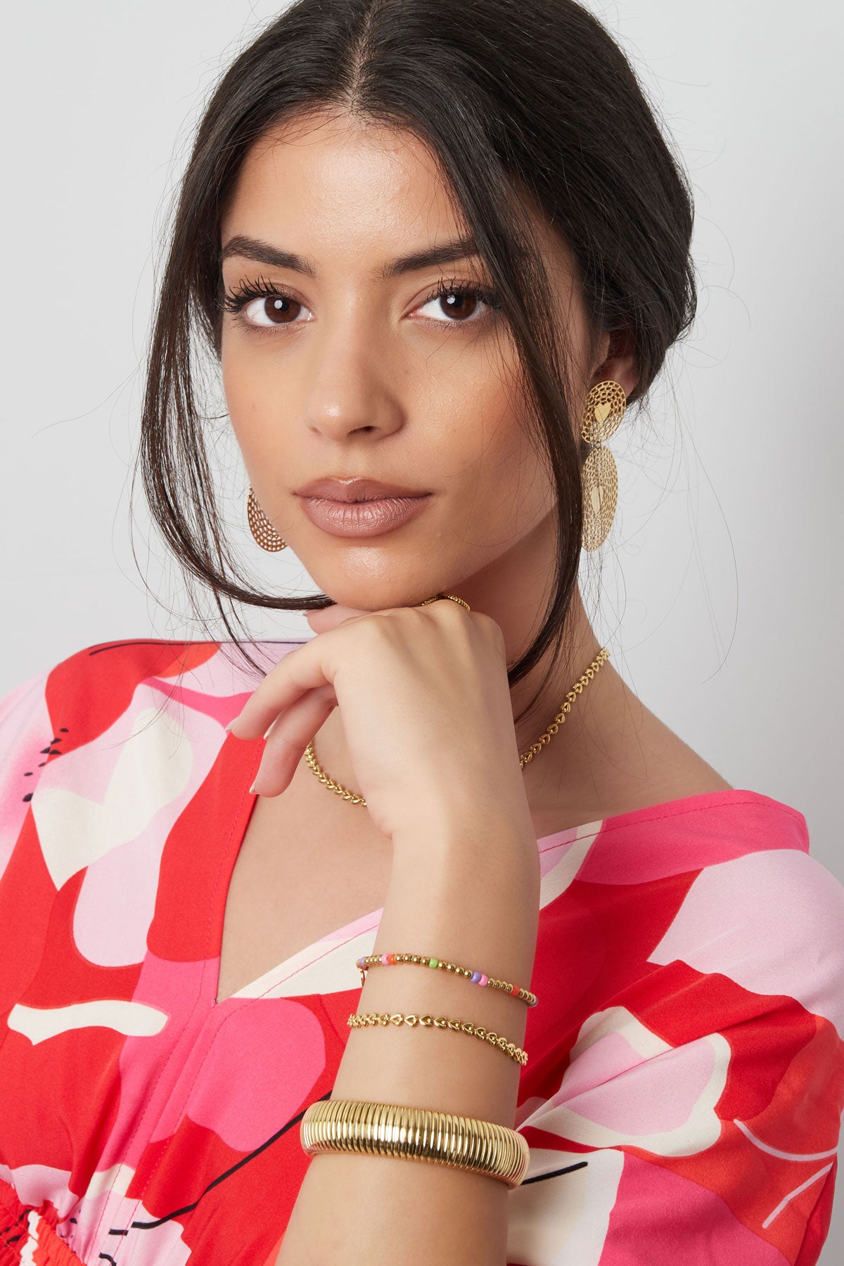 Woman wearing linked heart bracelet on her wrist along with colorful beaded and gold bangles, dressed in pink and red floral top