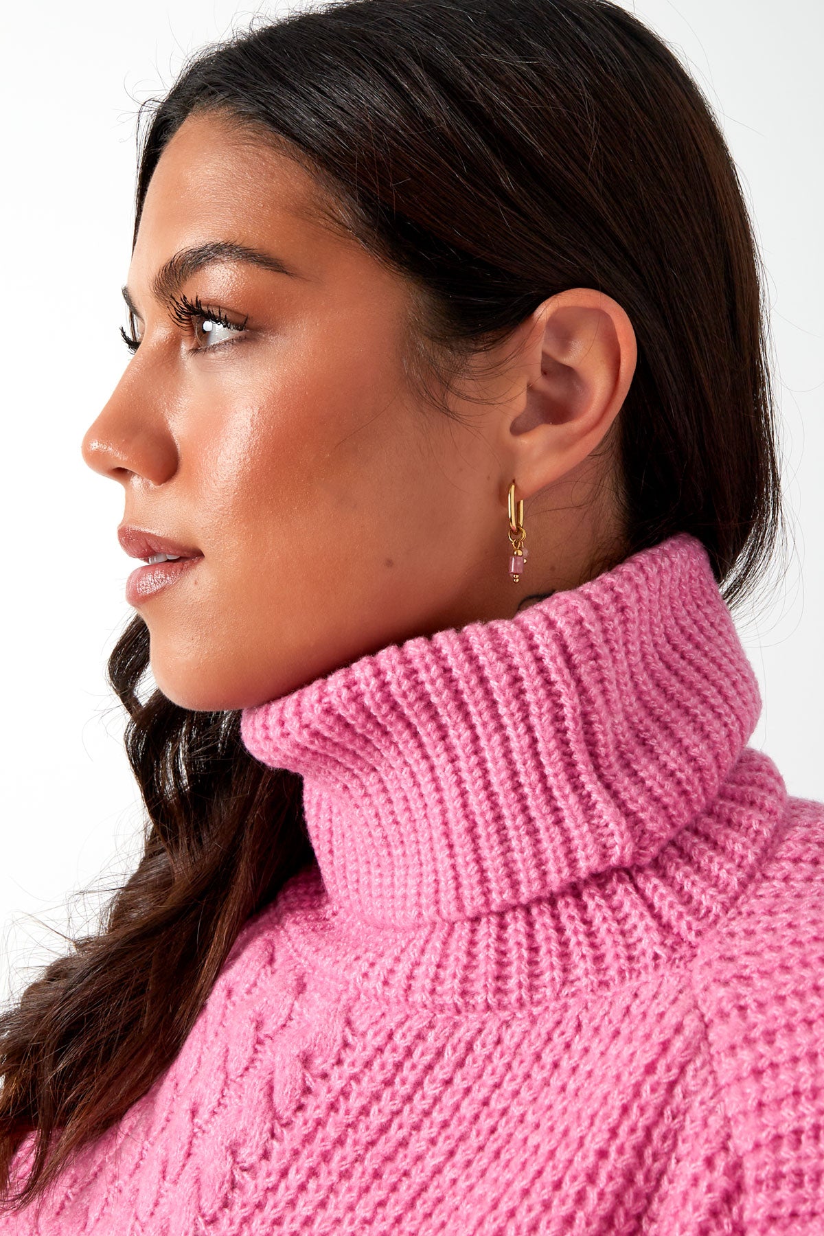 Side profile of woman with pink turtleneck sweater wearing gold hoop earrings with pink stone charm