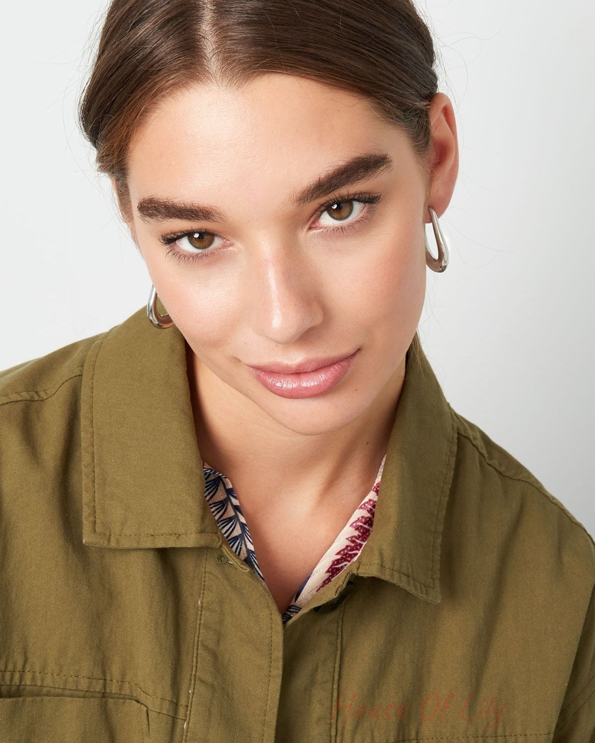 Model wearing silver teardrop hoop earrings, front-facing with playful gaze and olive green jacket