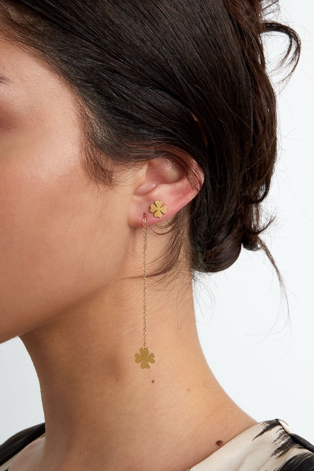 Close-up of woman wearing one gold-tone four leaf clover stud earring paired with a long chain drop earring