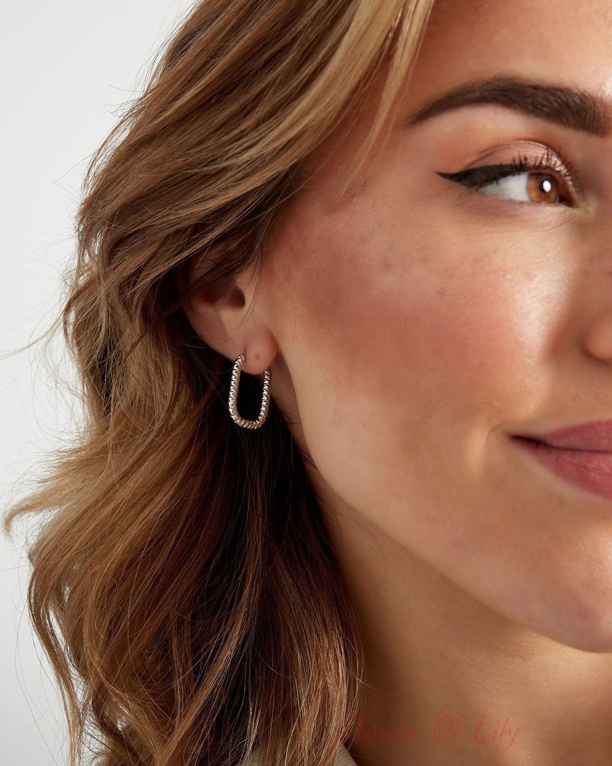 Angled close-up of model smiling wearing silver textured oval hoop earrings