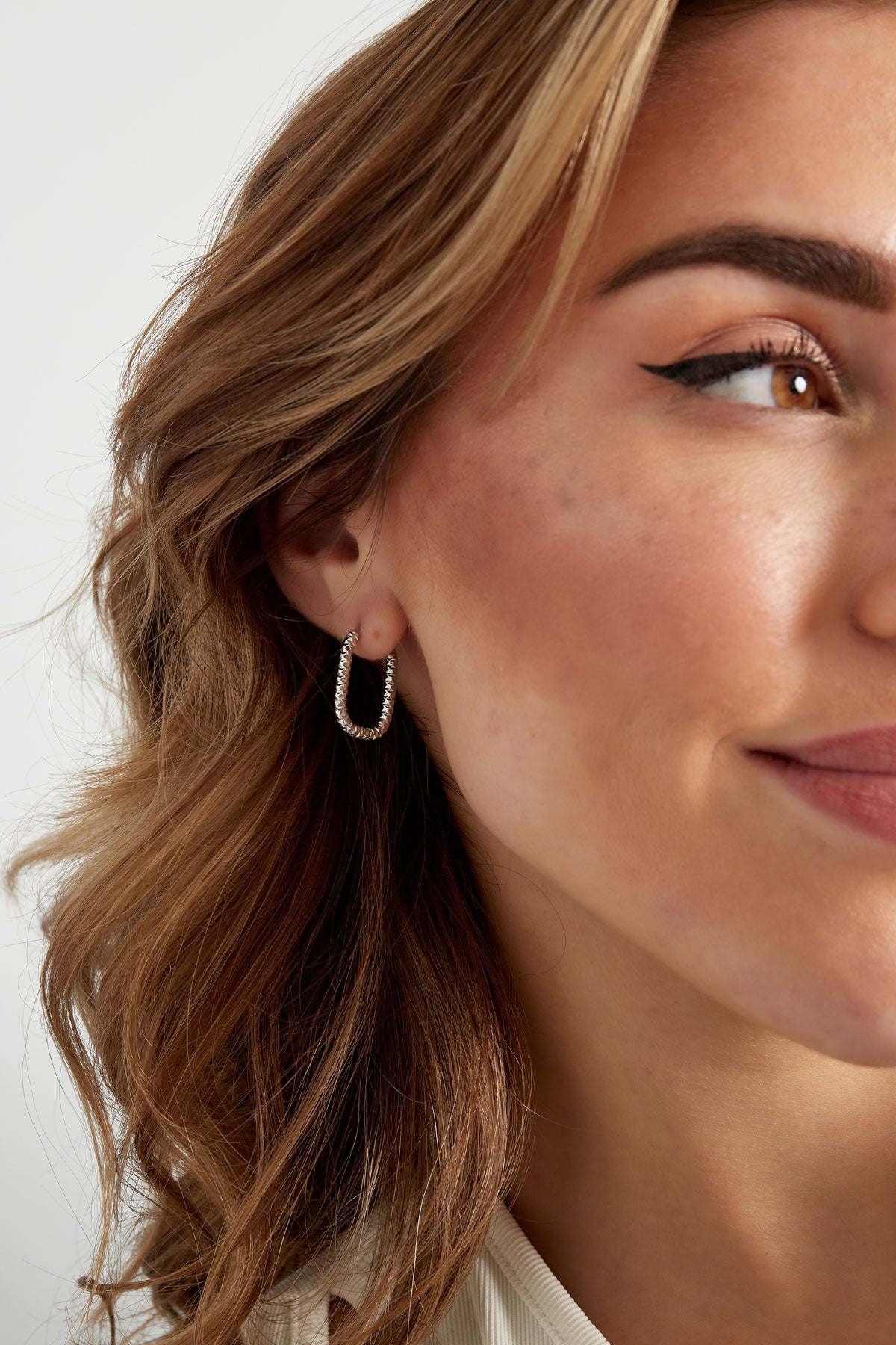 Angled close-up of model smiling wearing silver textured oval hoop earrings