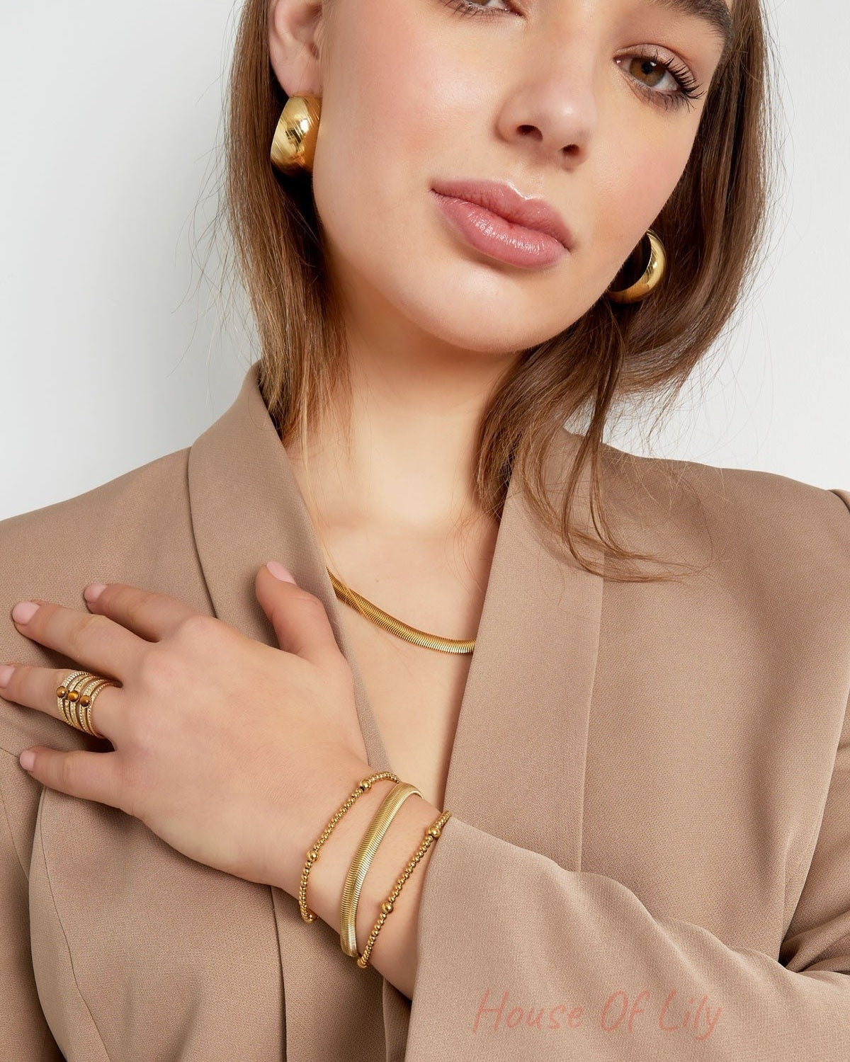 Woman showcasing gold chain bracelet along with matching ring and earrings in beige blazer