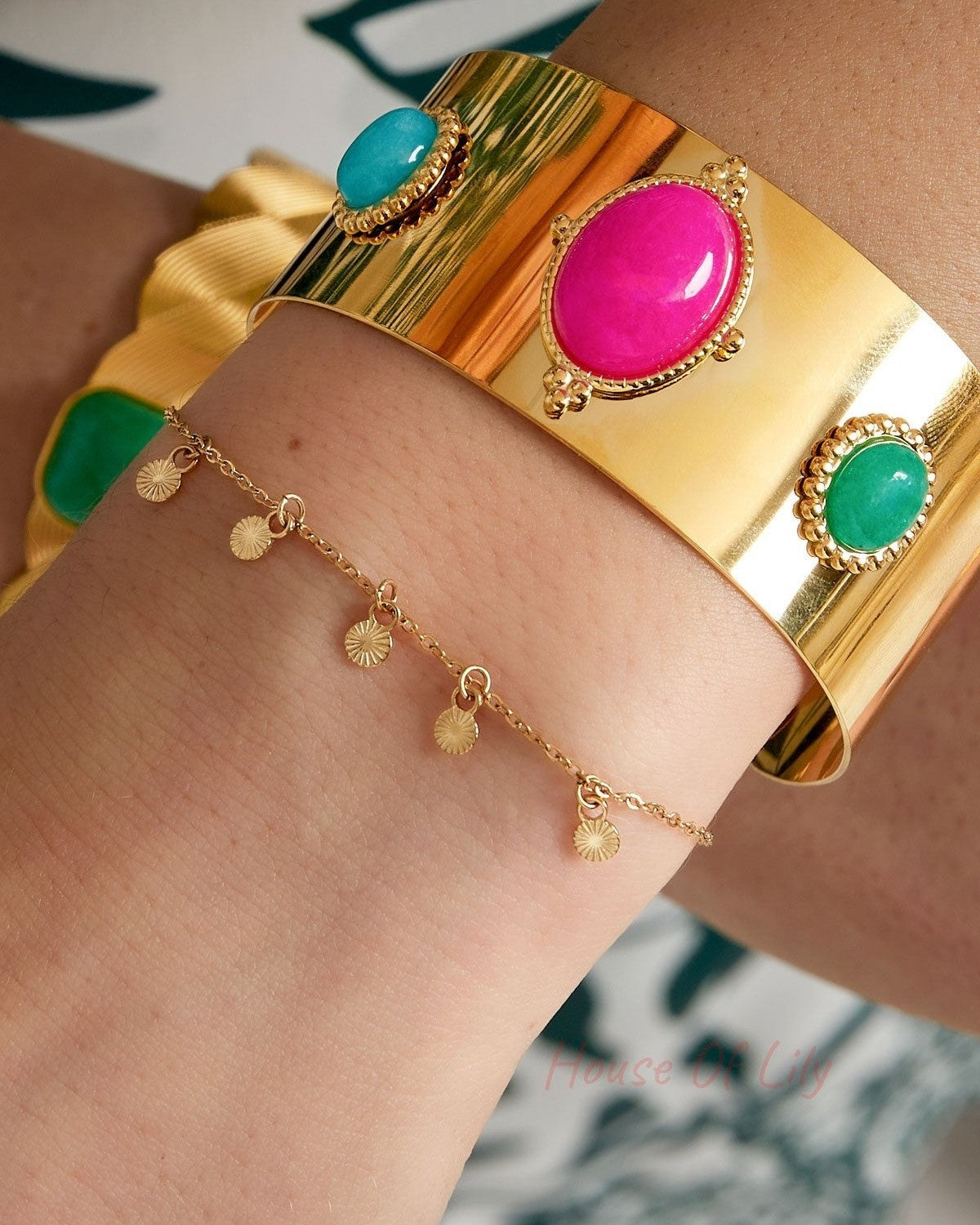 Wrist adorned with gold disc charm bracelet paired with a bold, colourful wide cuff bracelet featuring large stones
