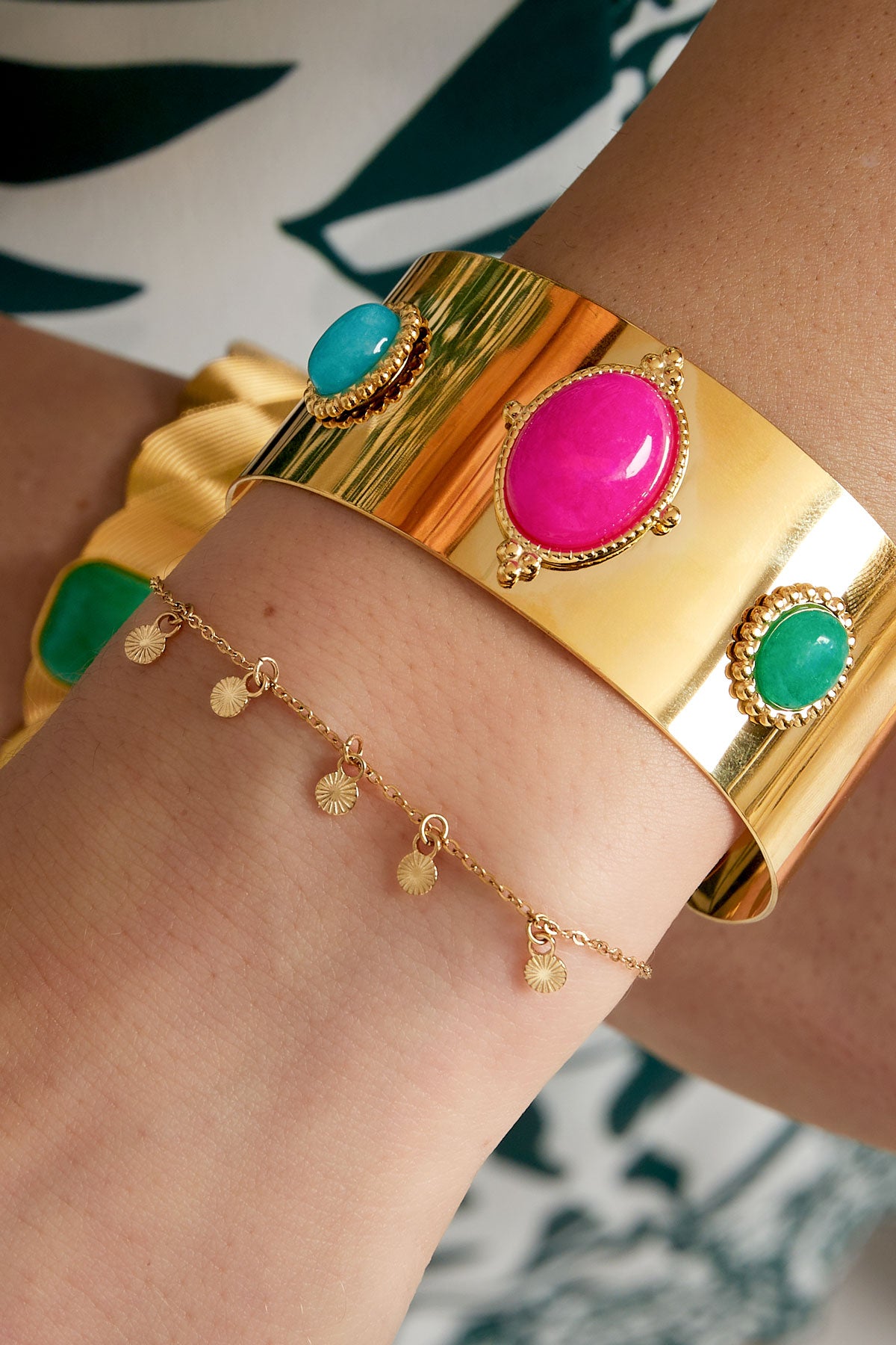 Wrist adorned with gold disc charm bracelet paired with a bold, colourful wide cuff bracelet featuring large stones