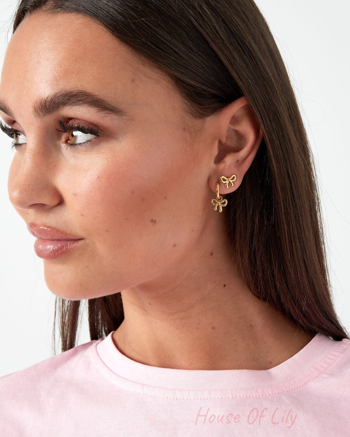Woman wearing gold bow knot stud earrings paired with a gold bow knot hoop earring, looking to the side