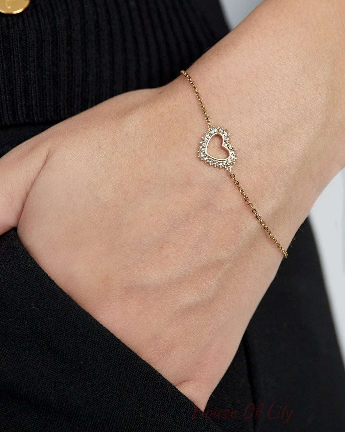 Close-up of a woman wearing a gold-tone heart charm bracelet with rhinestones on her wrist showcasing its delicate design