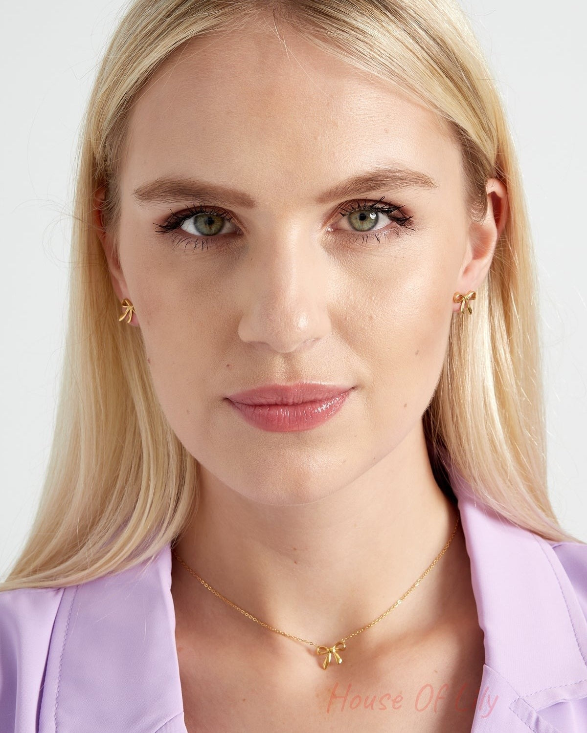 Front view of woman wearing gold bow stud earrings and matching necklace with lavender blazer