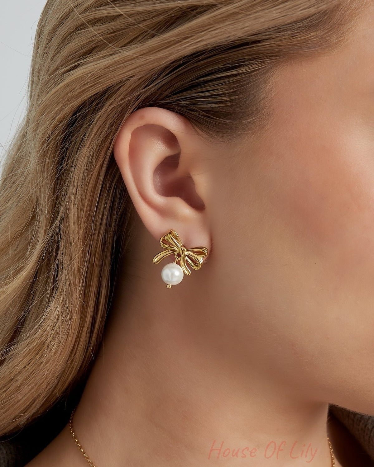 Close-up of woman wearing gold bow earrings with pearl drops showing youthful, minimal style