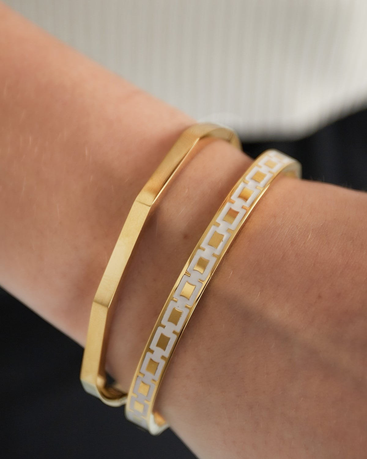 Close-up of wrist wearing two bracelets: gold hexagon bangle and white and gold patterned bracelet
