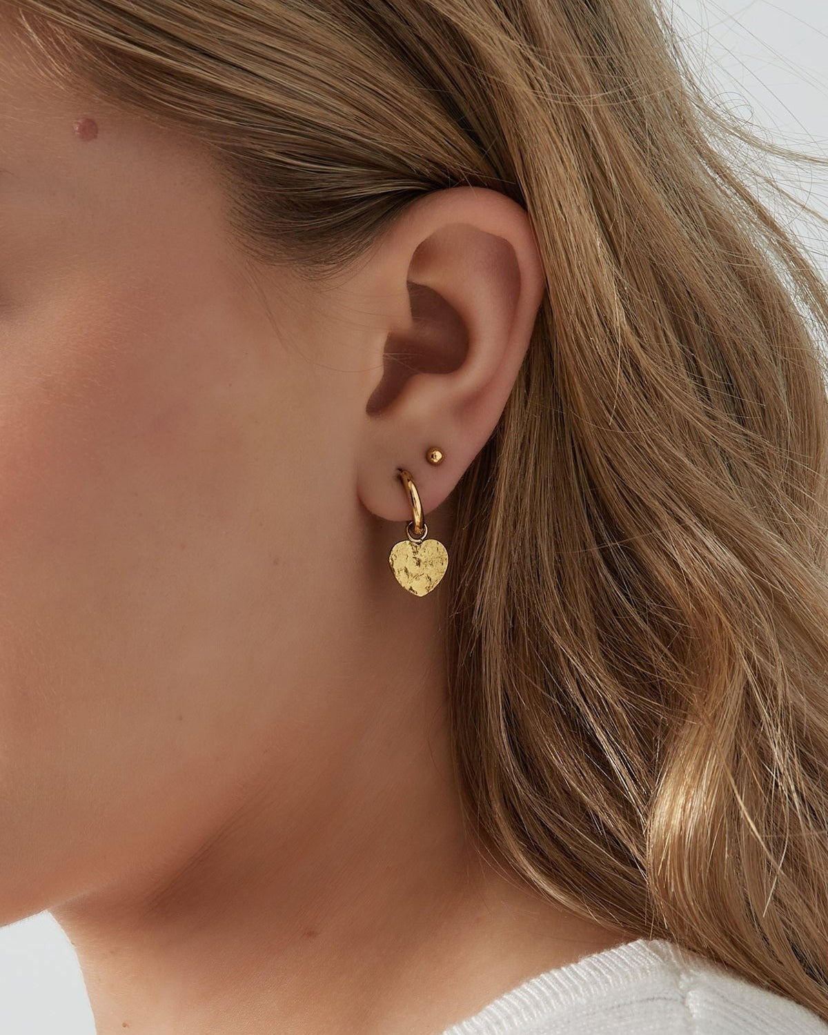 Close-up of woman wearing gold textured heart hoop earring