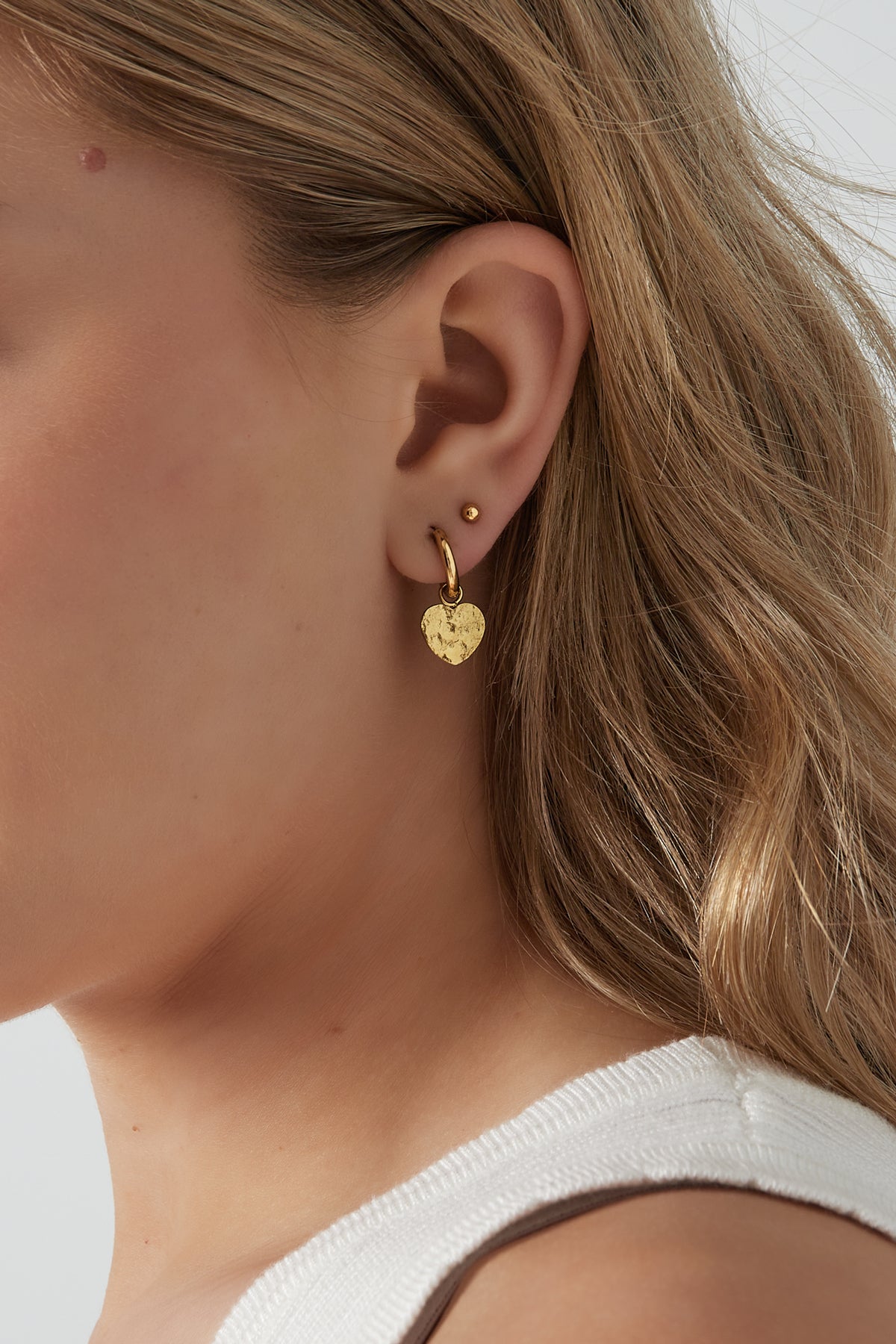Close-up of woman wearing gold textured heart hoop earring