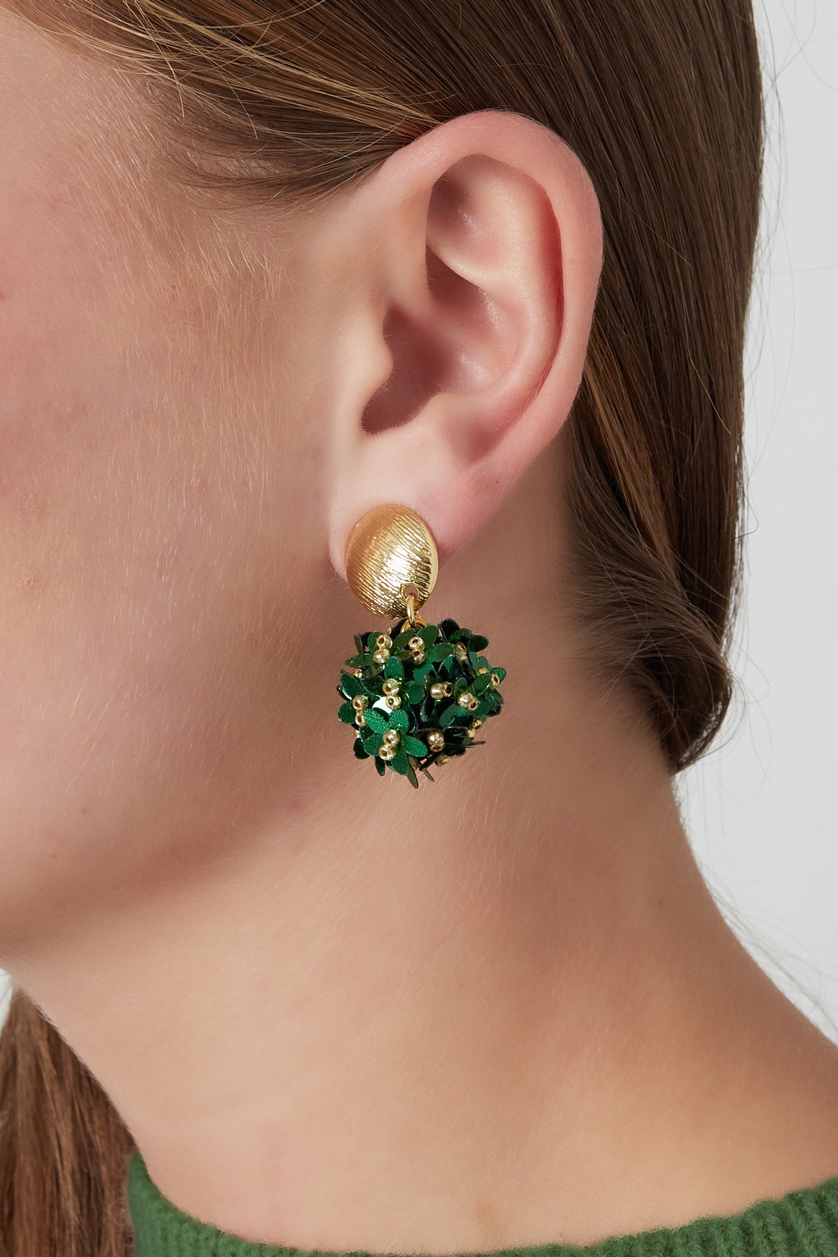 Side view of a woman's ear wearing floral drop earring with gold-tone textured stud and a cluster of green flowers accented with small golden beads.