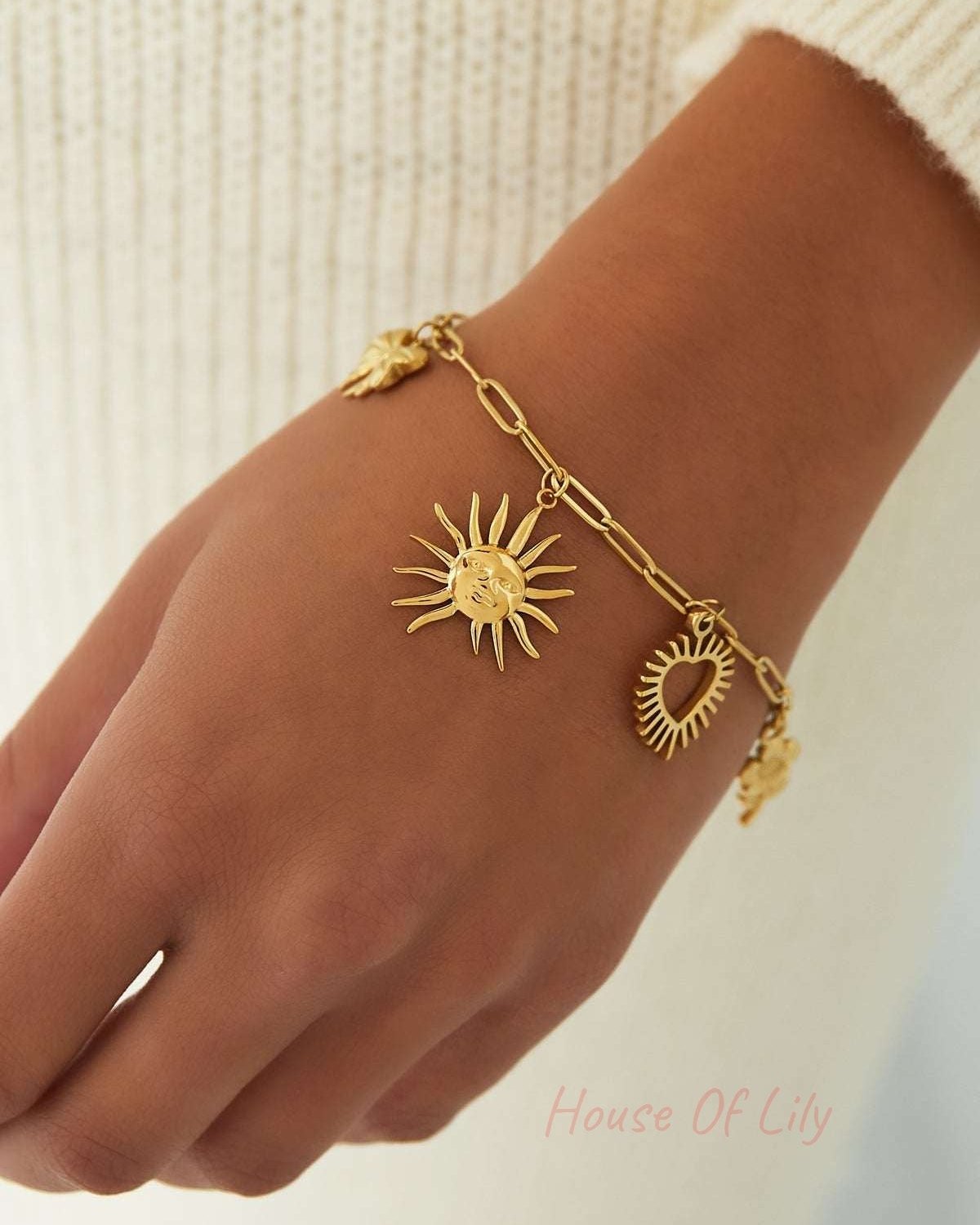 Close-up of gold-tone charm bracelet worn on wrist against soft cream sweater