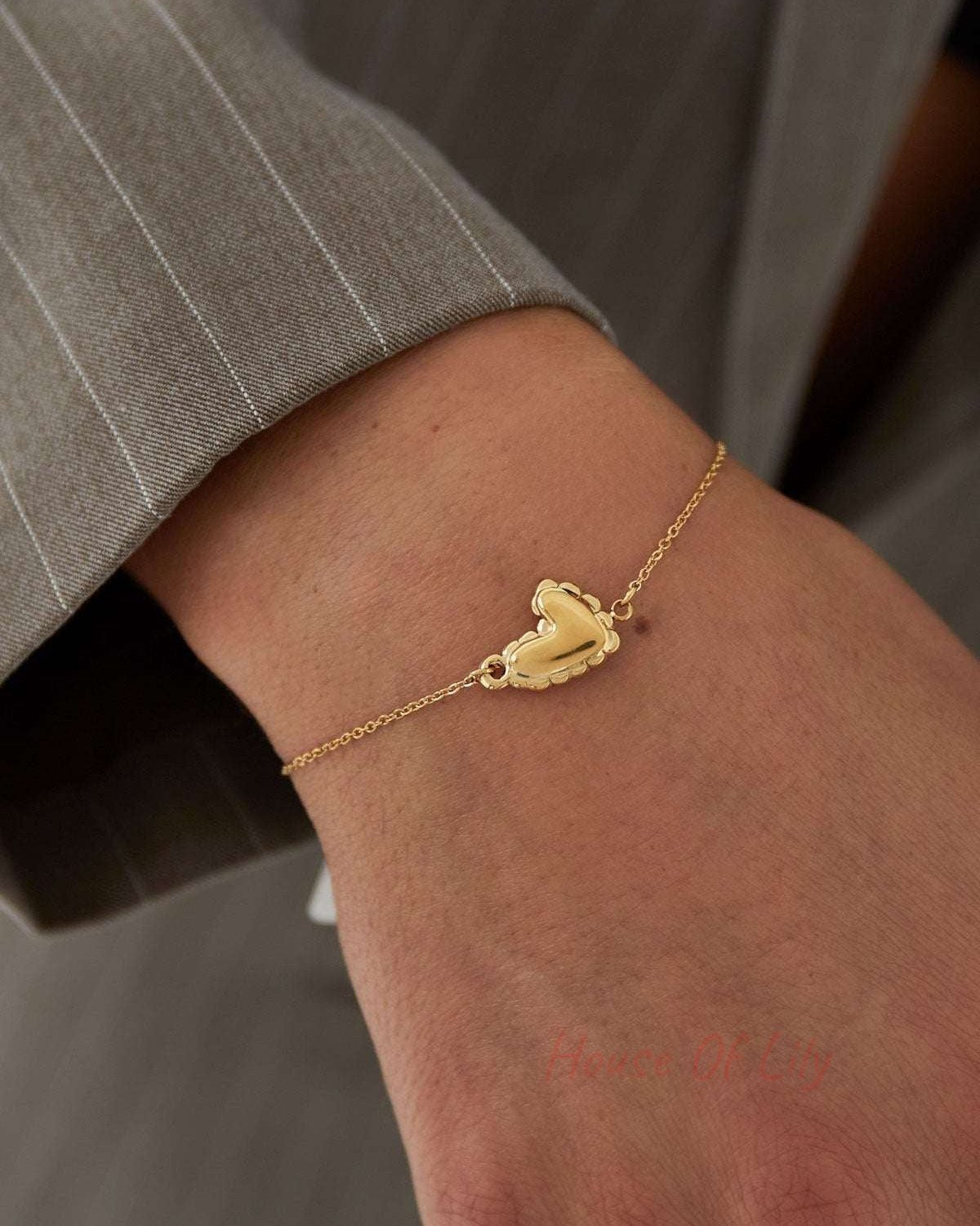 Close-up of gold heart bracelet worn on wrist with grey pinstripe sleeve visible