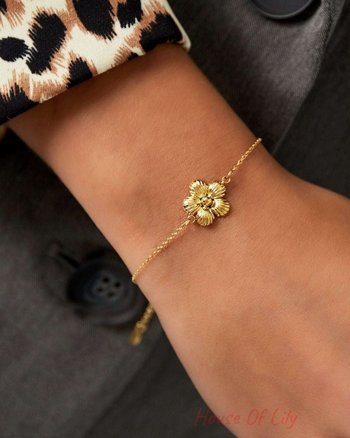 Close-up of gold daisy charm bracelet worn on wrist with leopard print sleeve and dark jacket showing elegant, youthful style