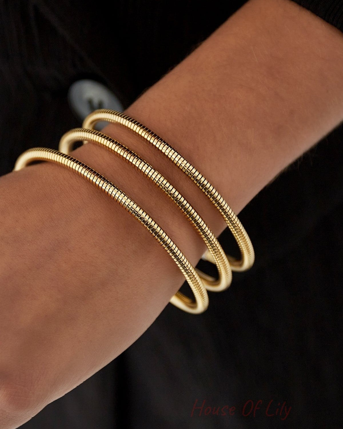 Close-up of a gold spiral coil cuff bracelet worn on wrist with black sleeve