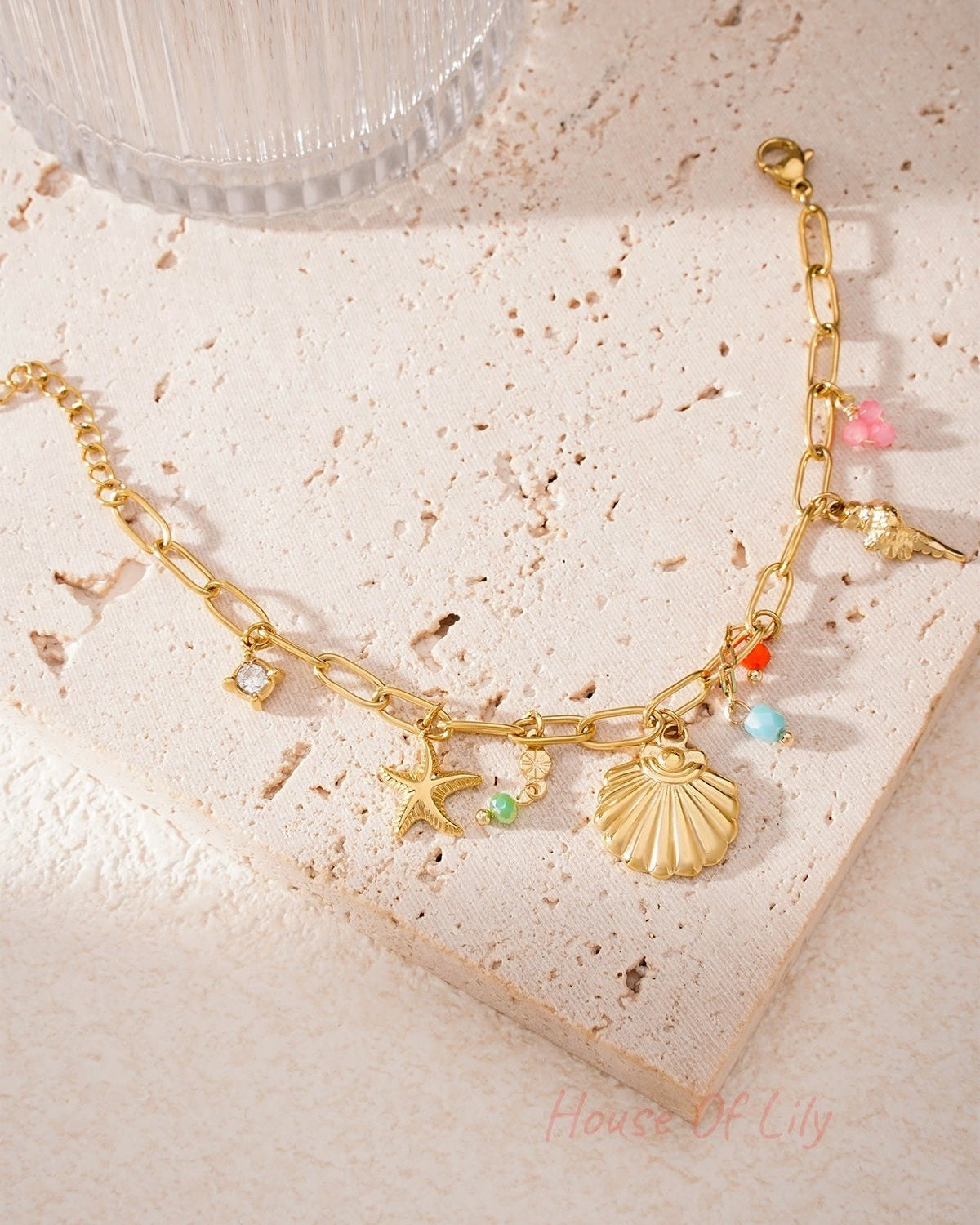 Golden sea charm bracelet laid flat on textured stone surface with sunlight highlighting colourful bead details