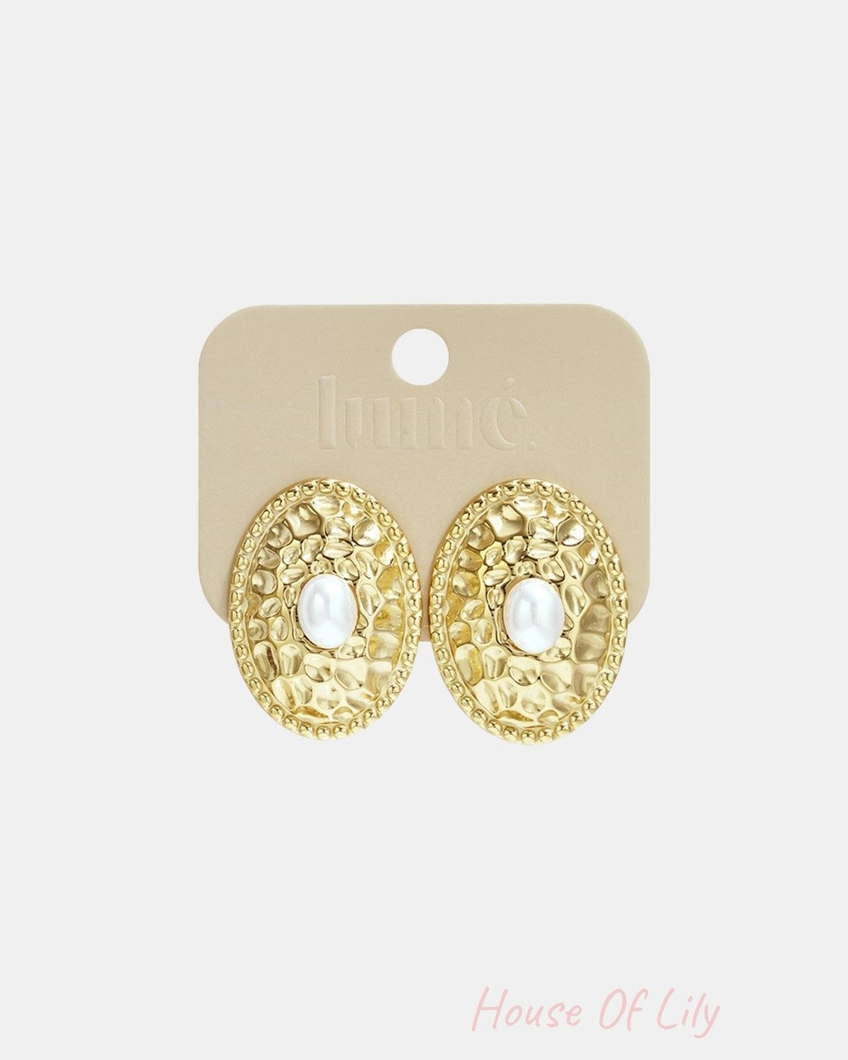 Gold-tone oval stud earrings with hammered texture and pearl center attached to beige Lumé branded card
