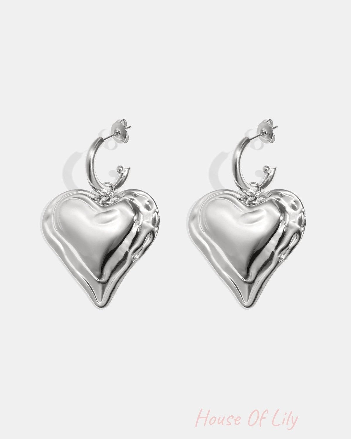 Close-up of chunky silver heart hoop earrings with rippled textured heart charms on white background
