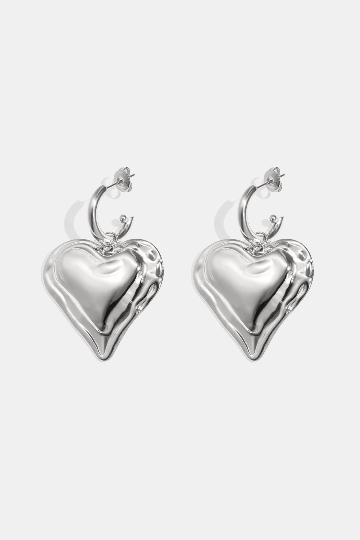 Close-up of chunky silver heart hoop earrings with rippled textured heart charms on white background