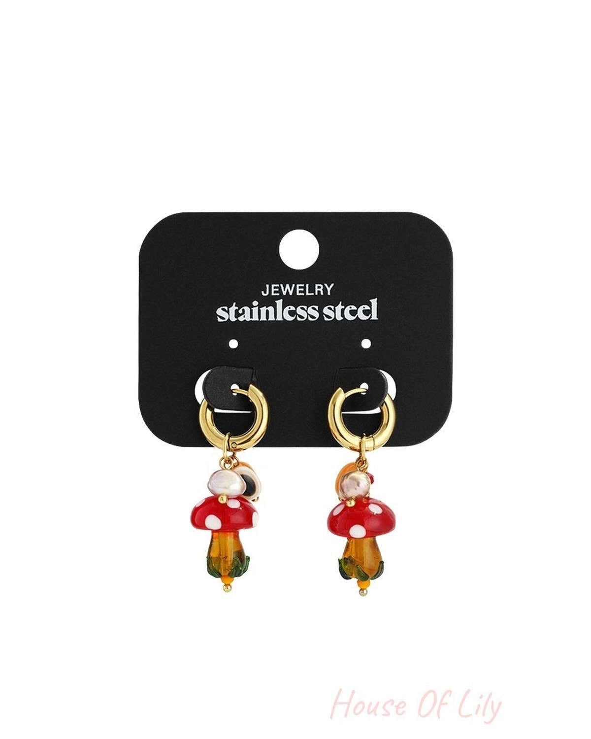 Gold stainless steel hoop earrings featuring dangling red-and-white mushroom charms with beads on a display card.
