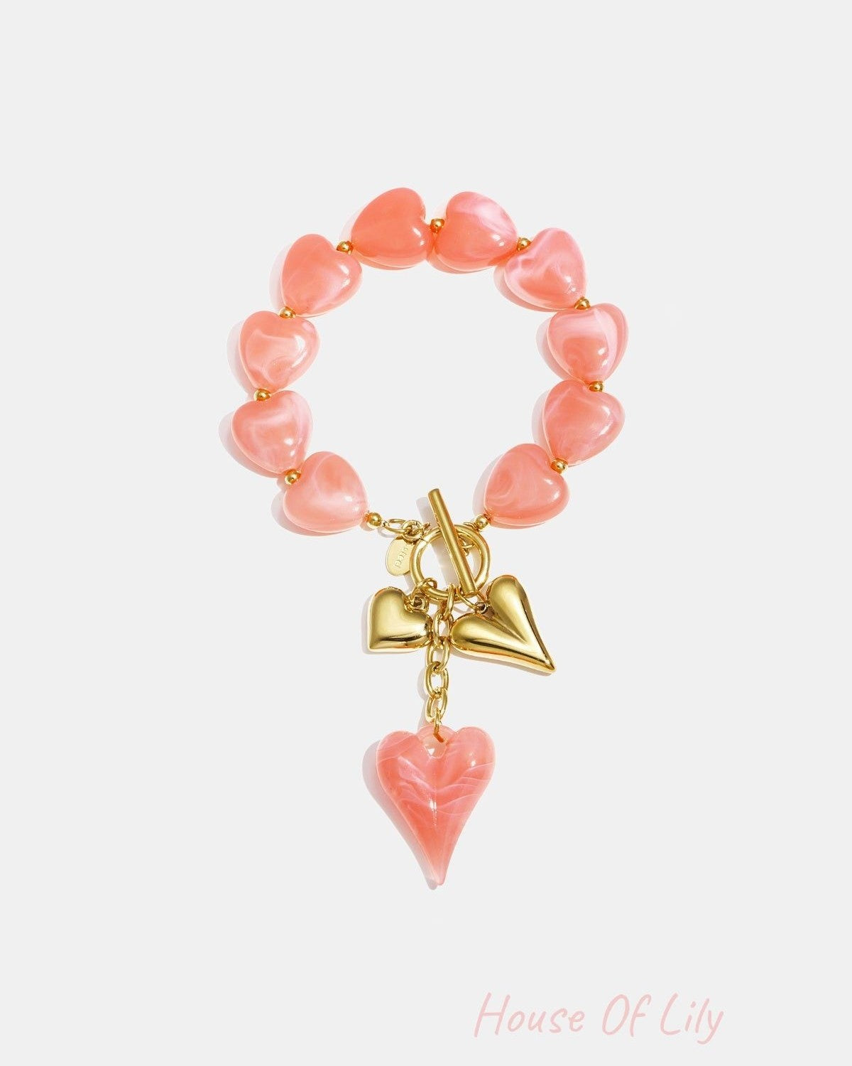 Close-up of blush pink heart-shaped acrylic beaded bracelet featuring gold heart charms and toggle clasp on white background