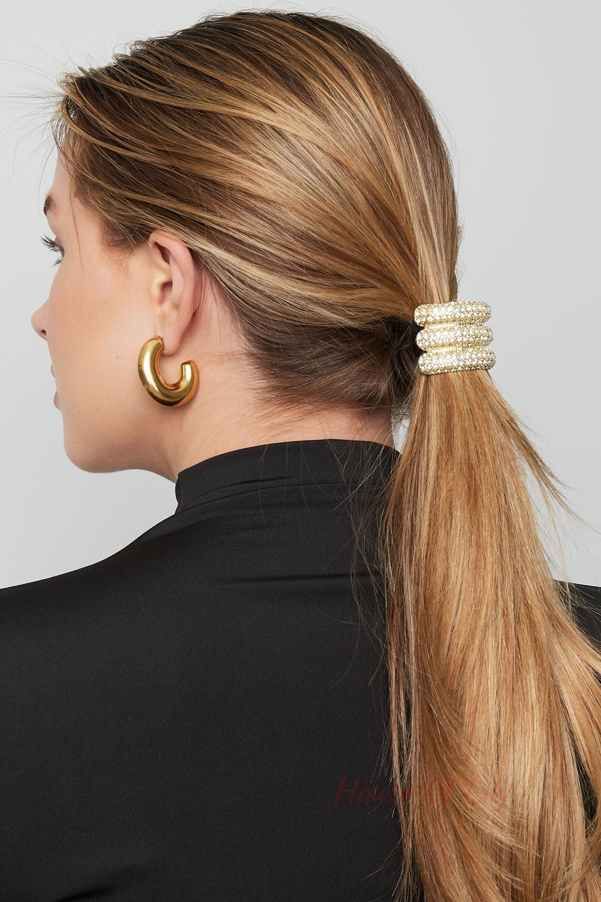 Side view of woman with blonde hair wearing the crystal gold-tone hair elastic securing a low ponytail, paired with chunky gold earrings