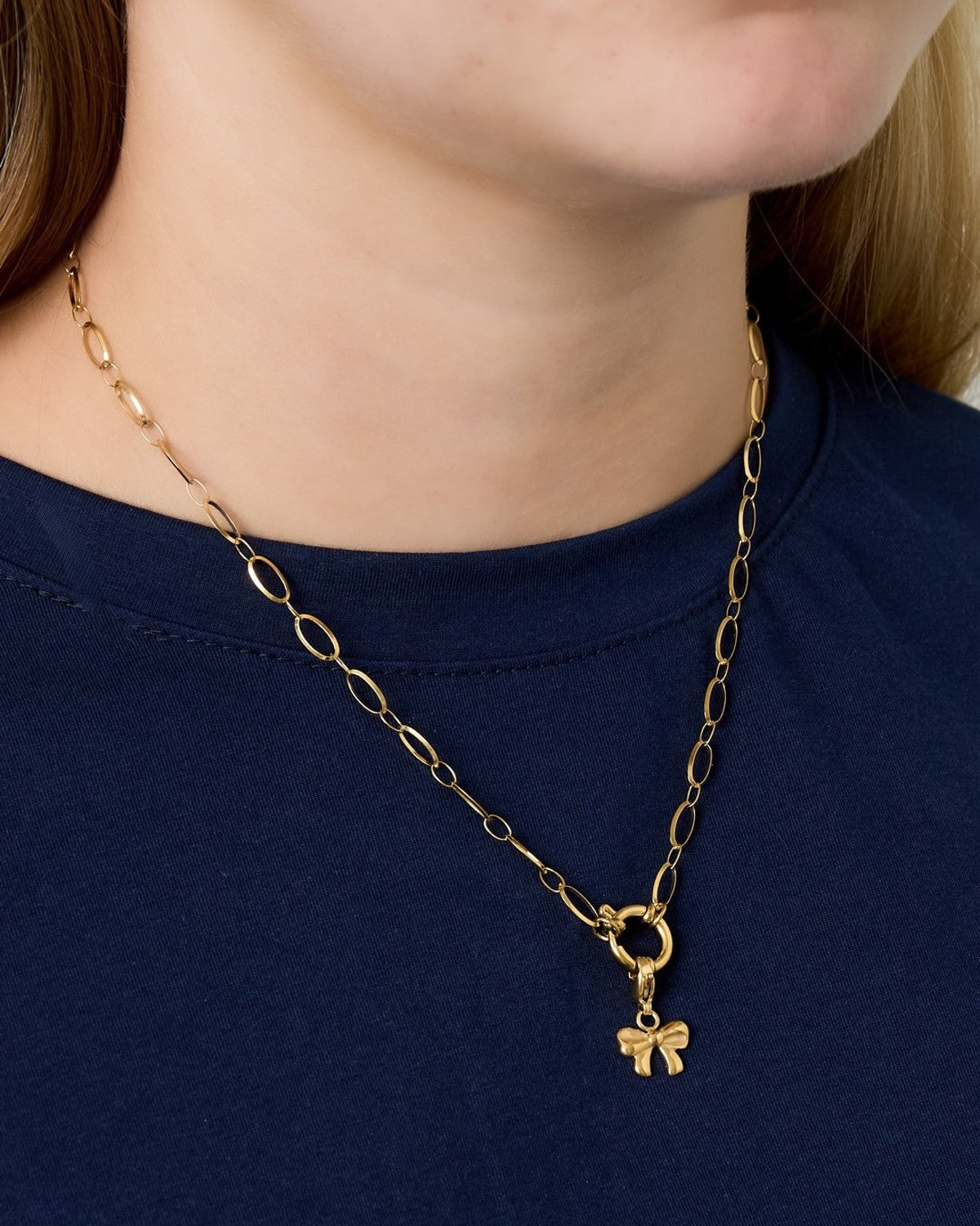 Model wearing gold link necklace with small gold bow charm pendant over a navy blue top
